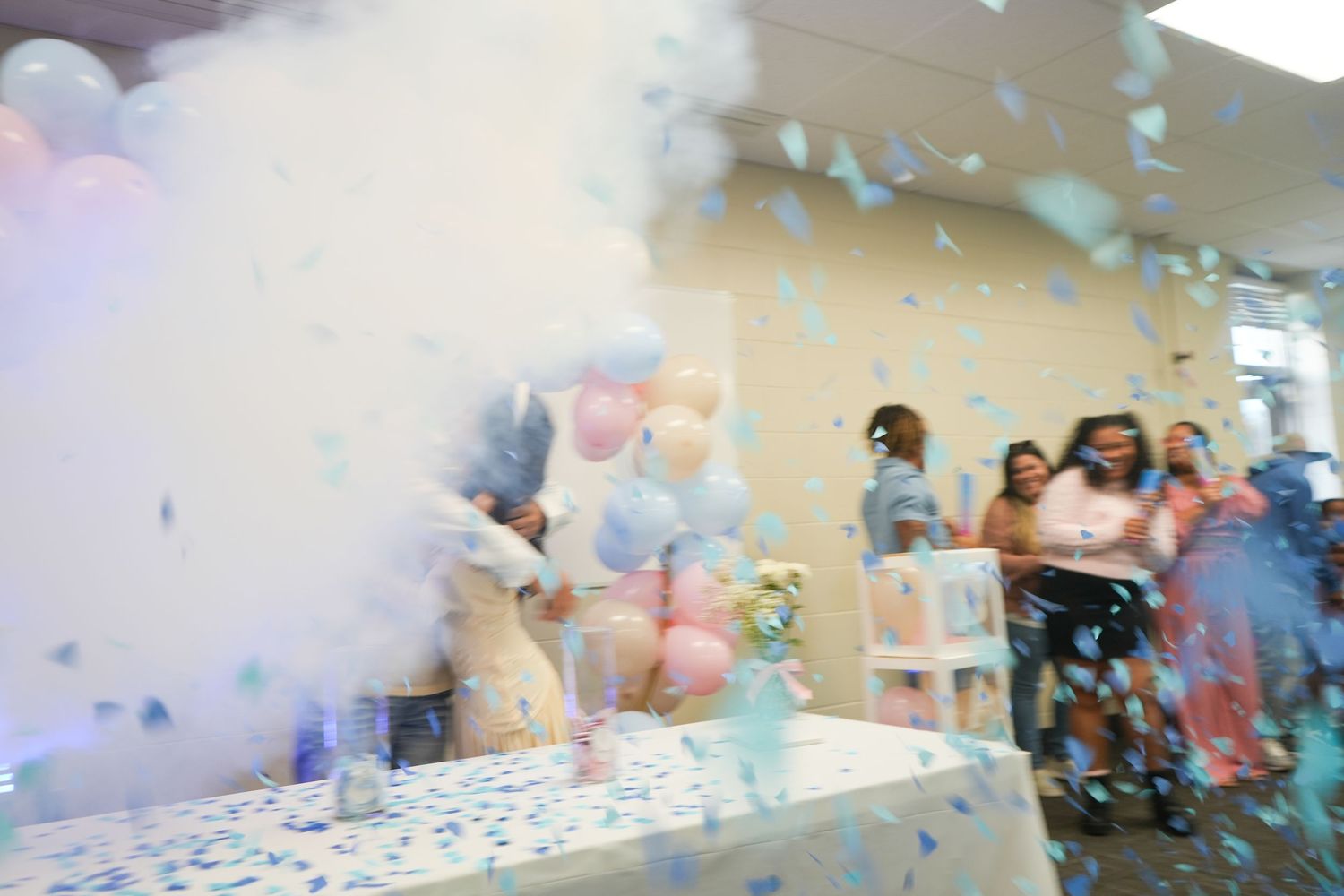 Gender reveal party with blue confetti explosion, balloons, and excited guests celebrating a baby boy announcement.