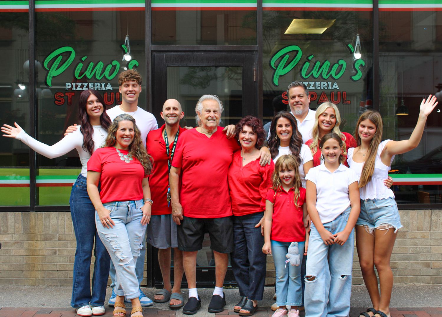 Family group photo smiling in front of Pino's Pizzeria restaurant entrance on a sunny day.