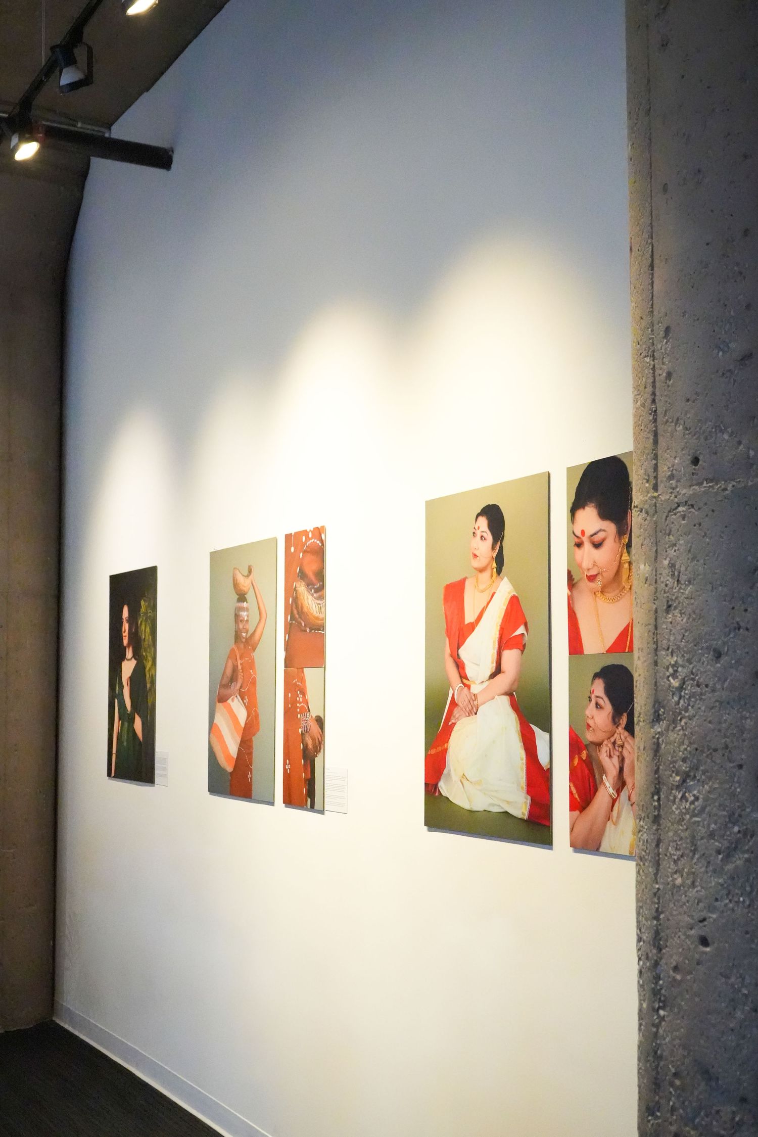 Art gallery wall displaying five photographs of a woman in traditional red and white Indian saree attire under spotlights.