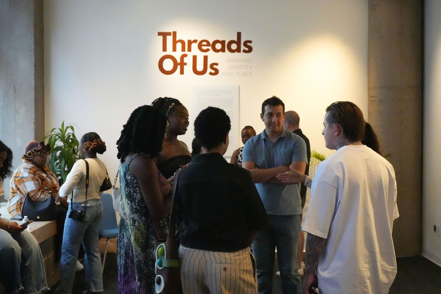 Visitors gather at the Threads Of Us exhibition opening, socializing in a modern gallery space.