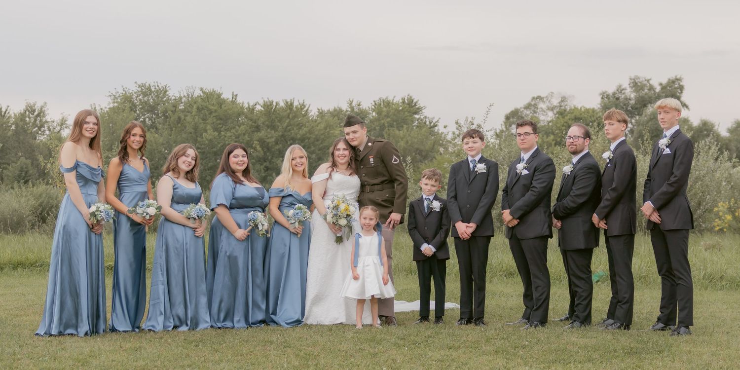 Wedding party stands in line on green lawn with bridesmaids in blue dresses.