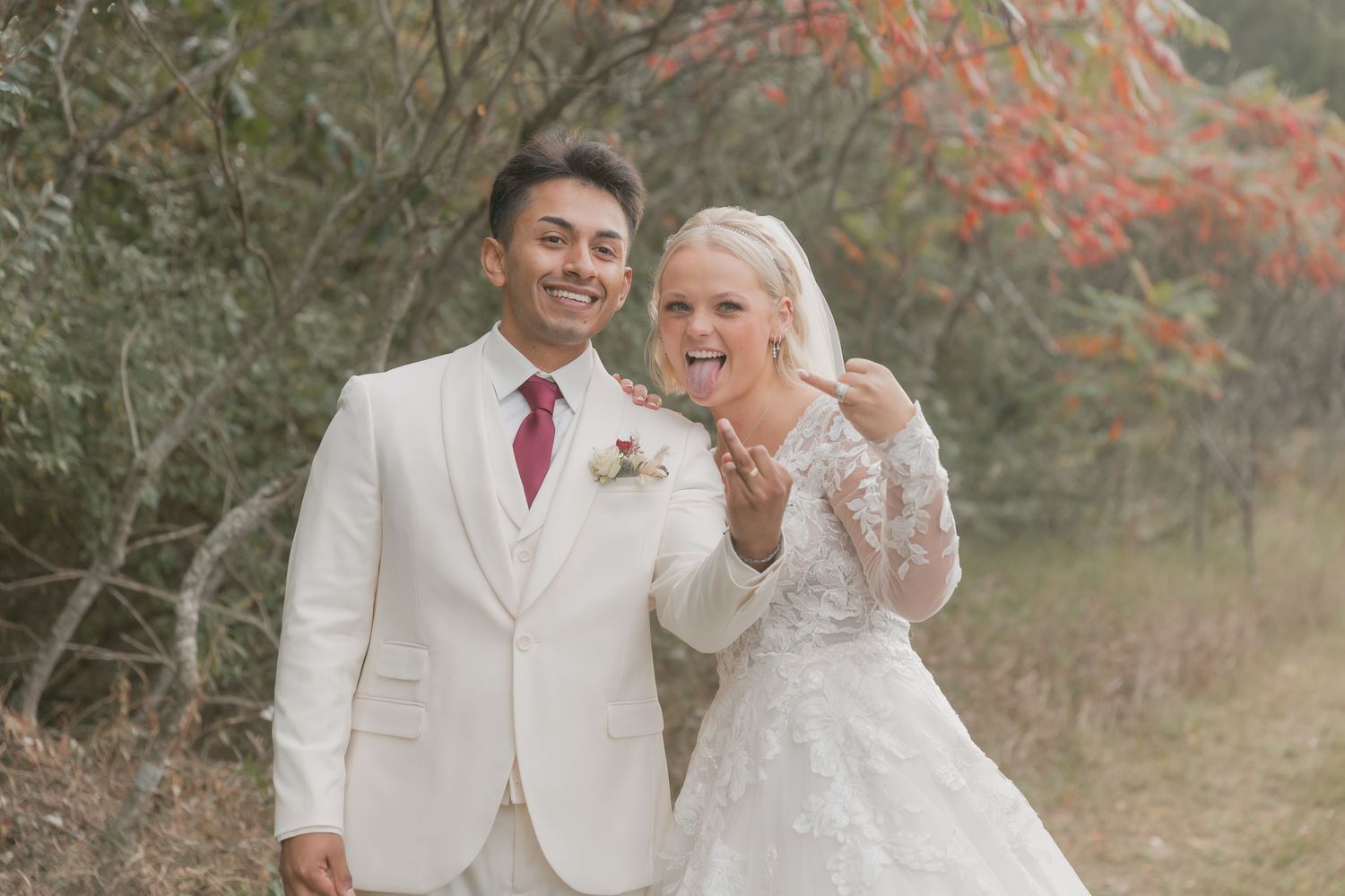Wedding couple in white attire walking together through a scenic fall landscape with red berries.