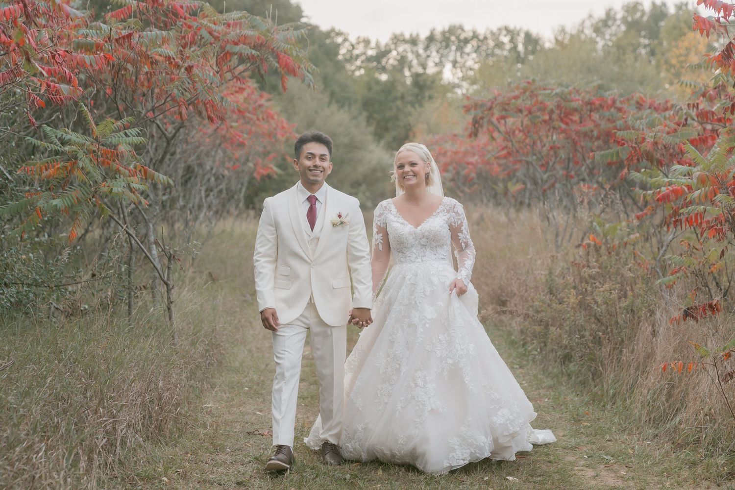 A romantic autumn wedding photoshoot featuring a couple posing among red berry bushes in a natural outdoor setting.