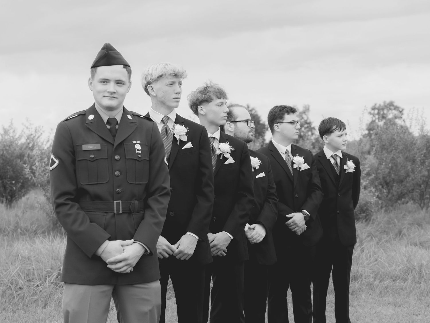 Vintage black and white photo of groomsmen lined up in formal attire with one in military uniform.