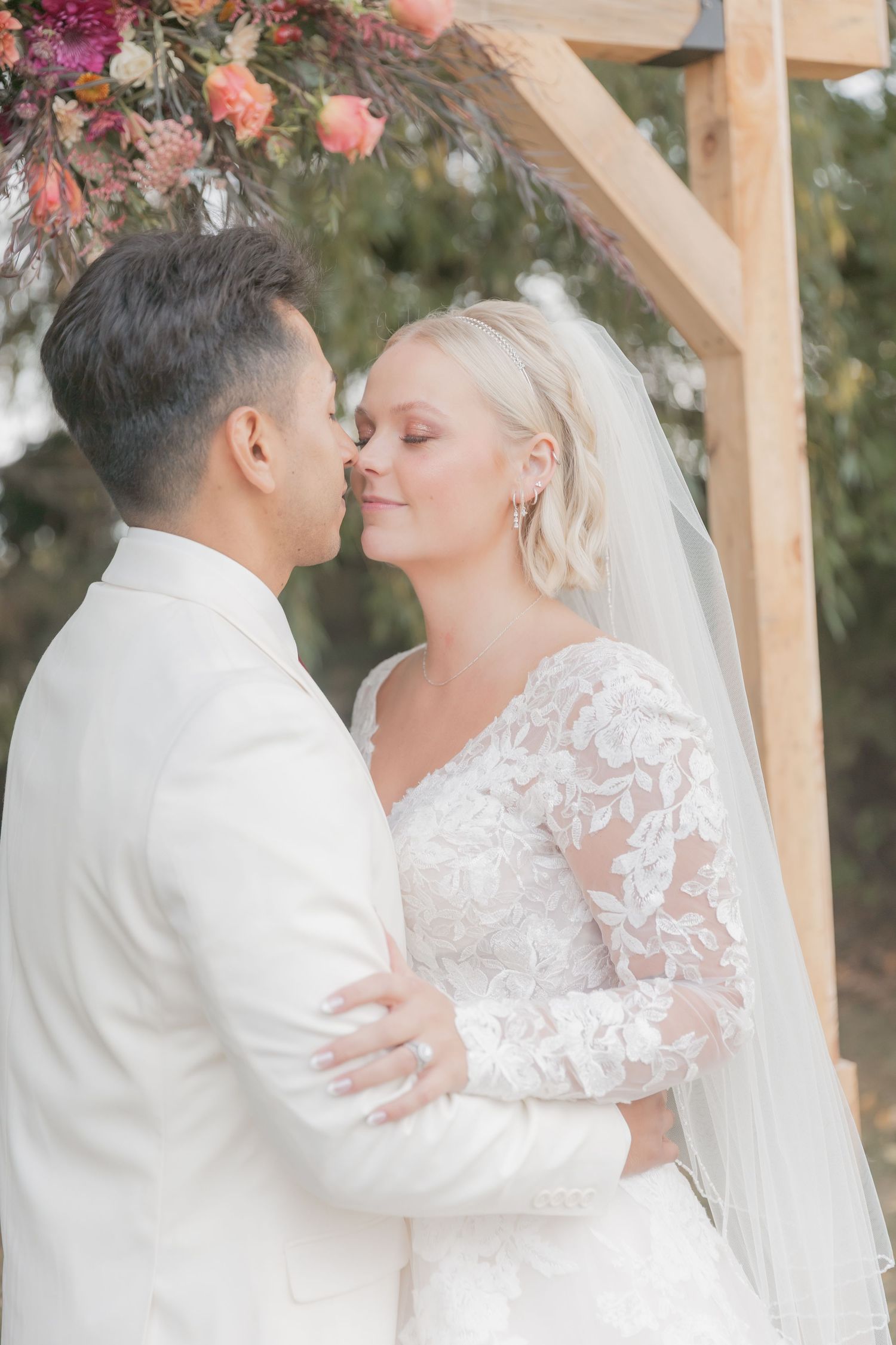 Newlyweds sharing intimate moment under floral arch during outdoor ceremony.