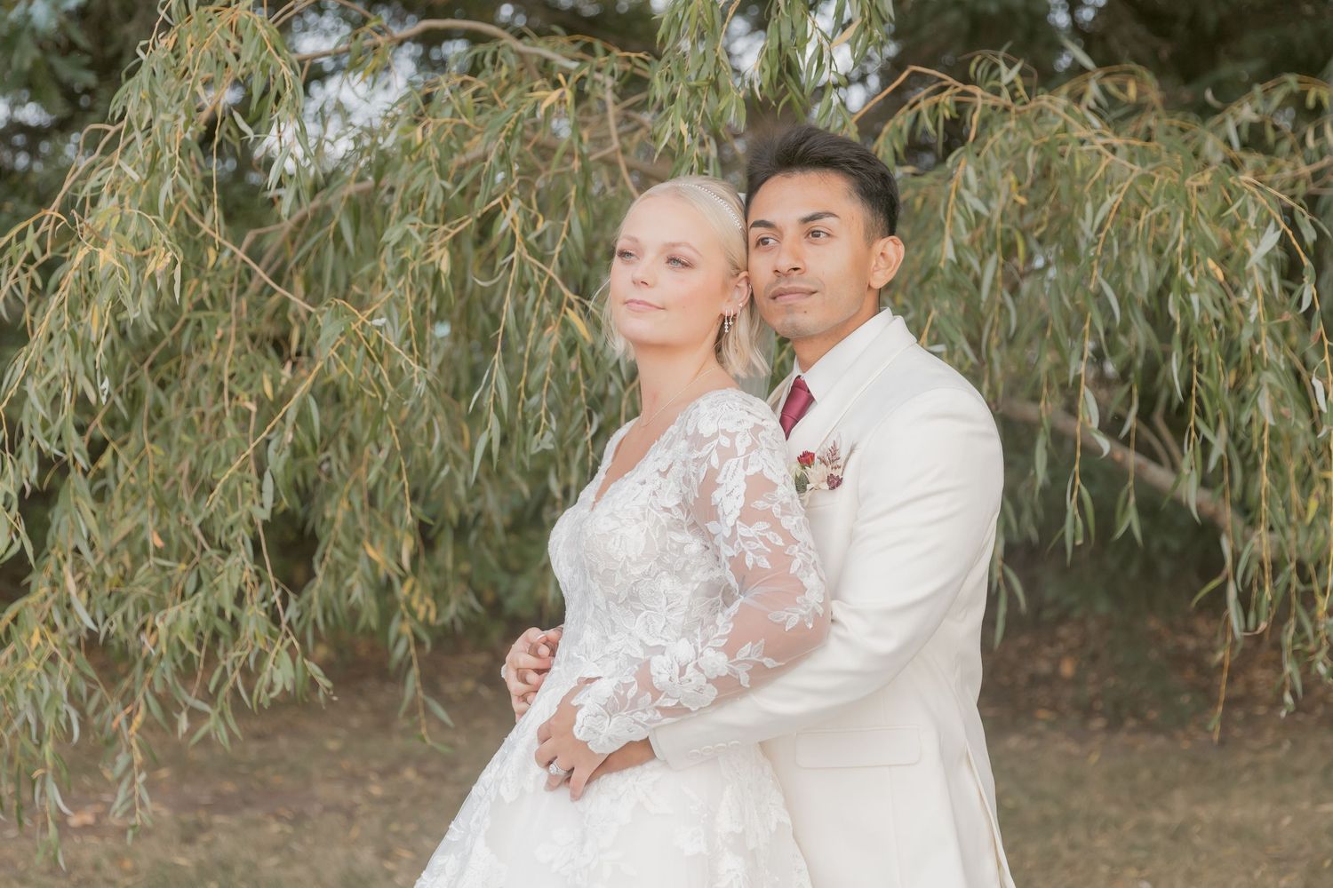 Romantic wedding portraits taken under drooping willow branches in natural lighting.