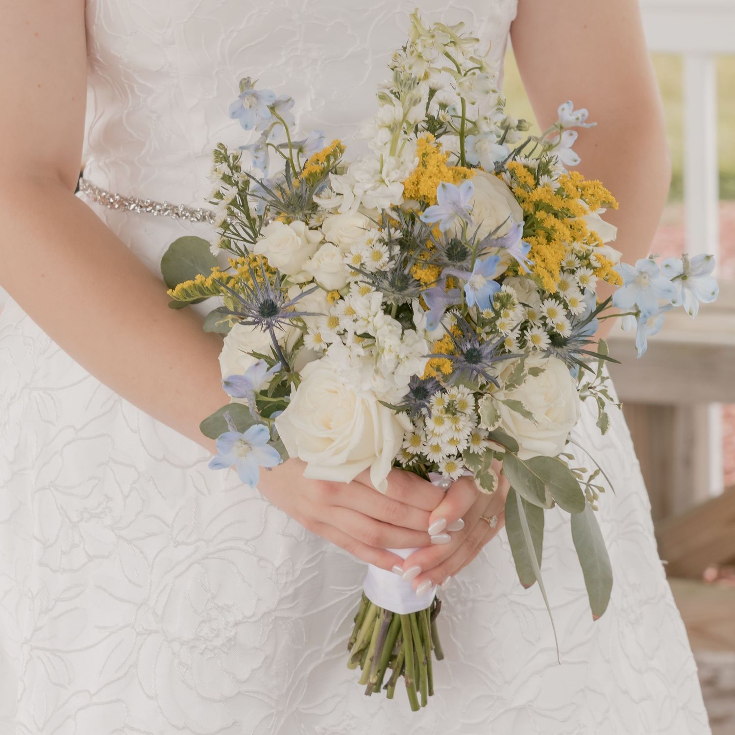 Close-up of a bridal bouquet with white roses, blue and yellow wildflowers, and eucalyptus.