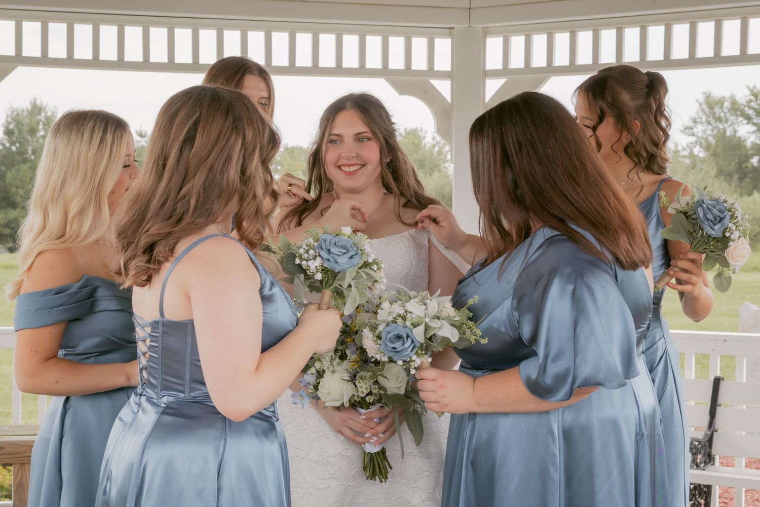 Wedding party sharing joyful moments in a gazebo with blue dresses and floral bouquets.