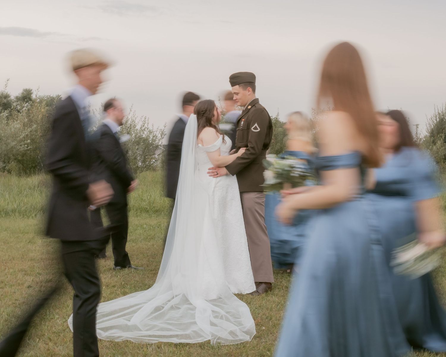 Wedding party members interact casually outdoors with bridesmaids in blue dresses.