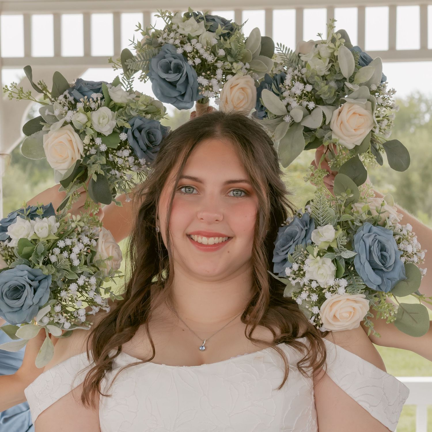 Bride poses under a floral arch with blue and pink roses in a white gazebo setting.