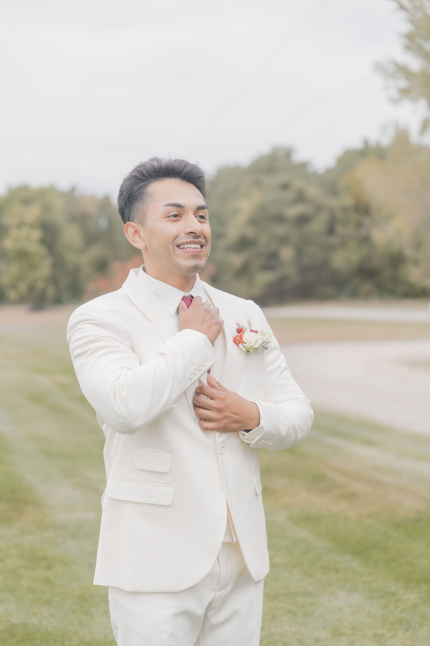 Groom in white suit showing joyful expressions during outdoor wedding photoshoot.