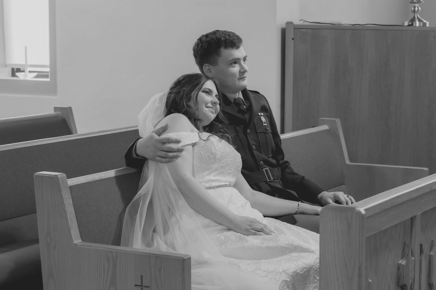 Black and white photo of couple sharing an intimate moment in church pews.