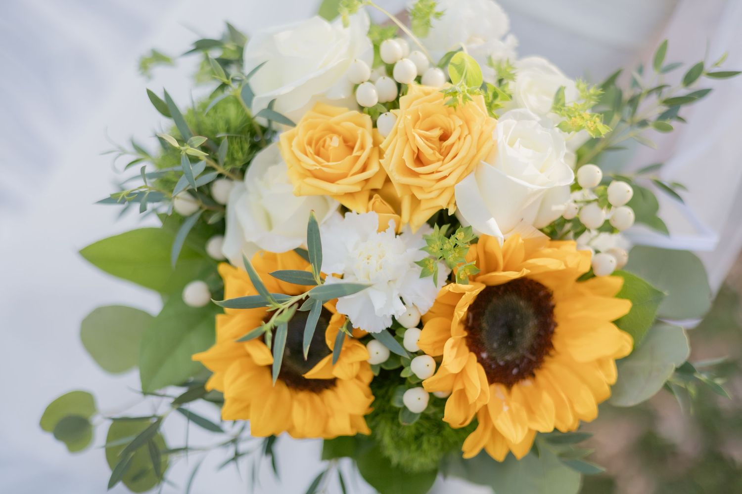 Wedding bouquet with bright sunflowers and yellow roses against a light background.