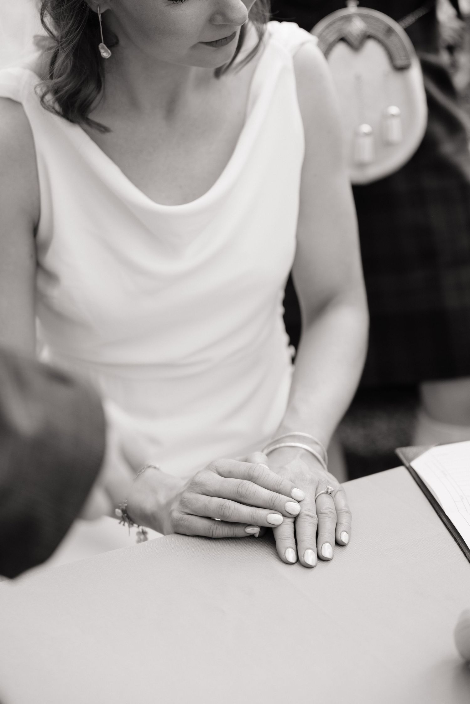 Bride in white dress with ring on finger resting hands on table during wedding ceremony signing.