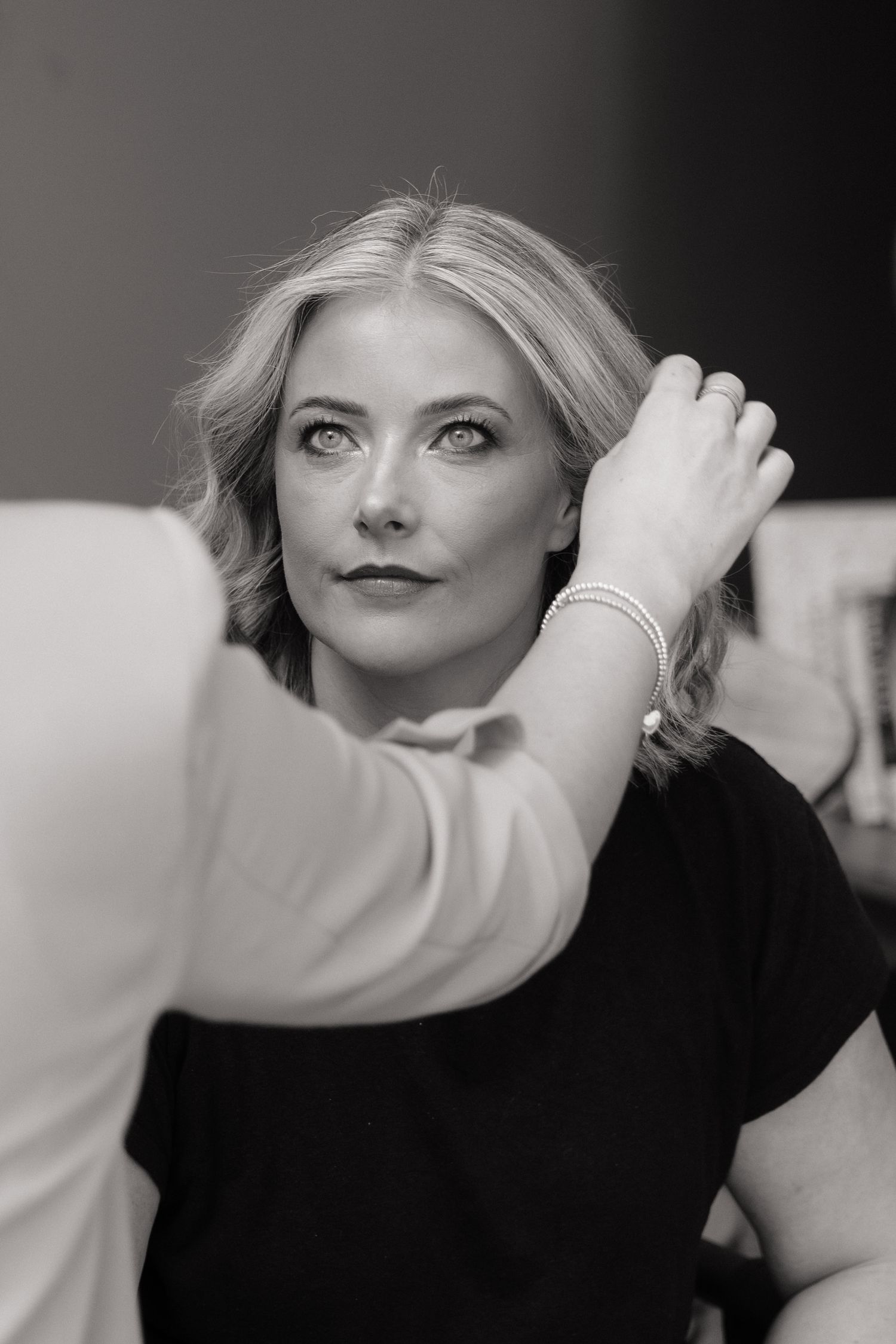 Black and white photo of a blonde woman getting her hair styled by a hairstylist in a professional setting.