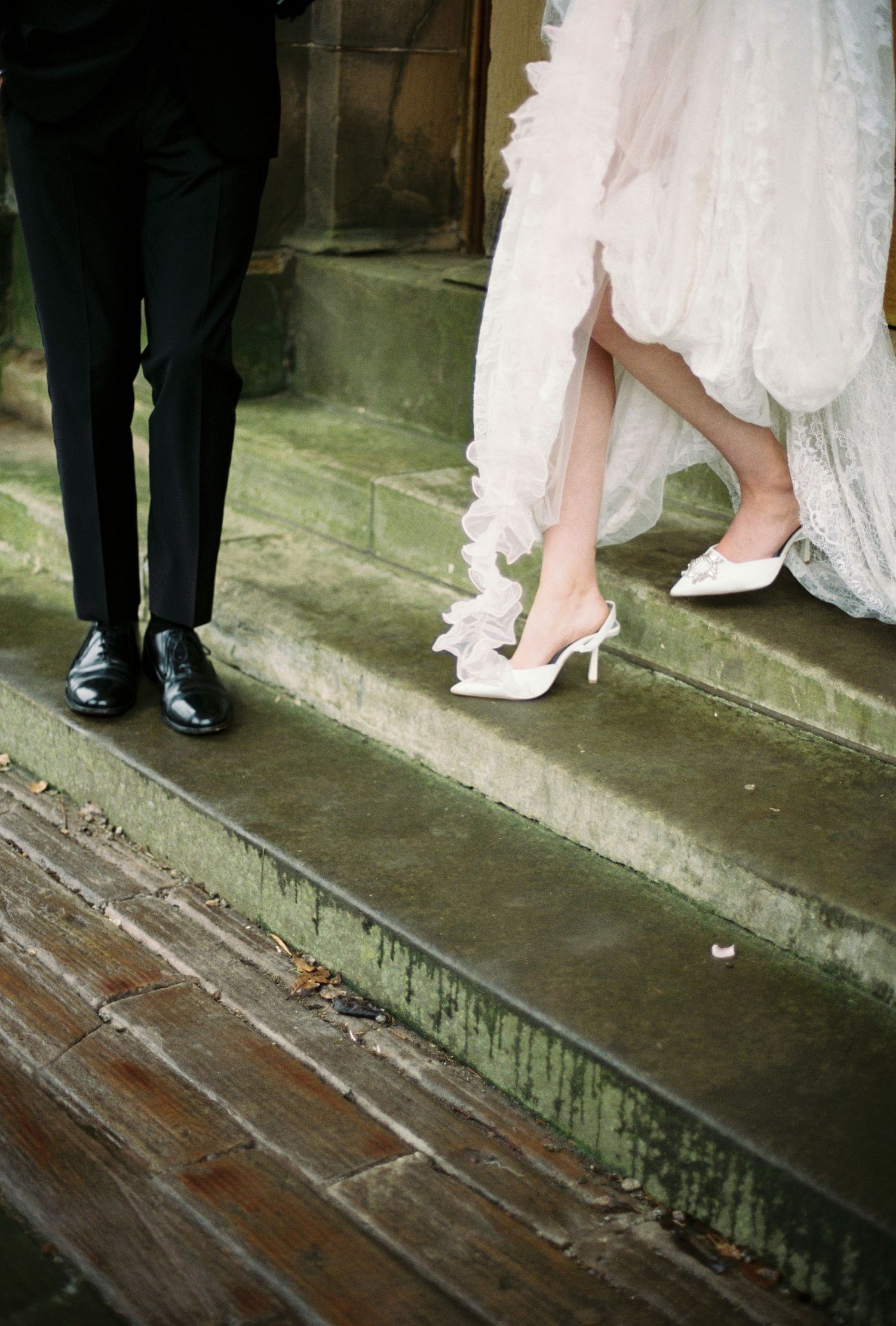A close-up view of a bride's white dress and the groom's black suit on a wooden staircase.