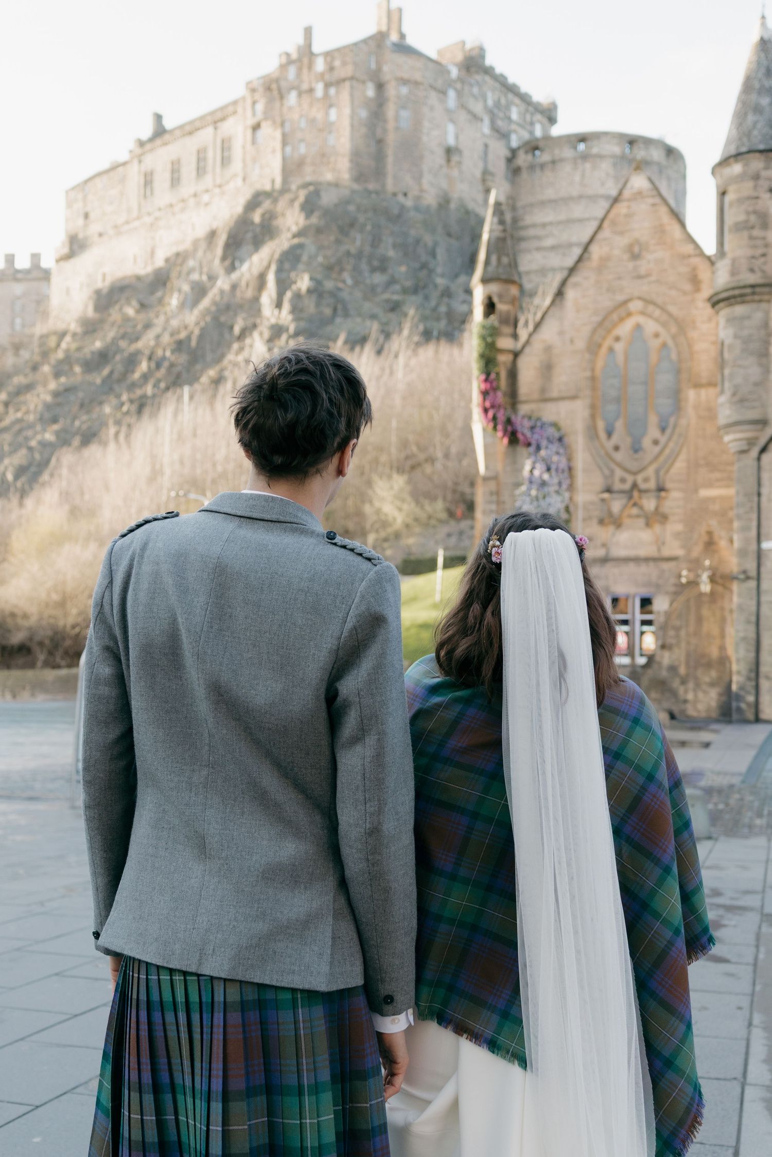 Couple in Scottish attire with kilt and tartan shawl views Edinburgh Castle on their wedding day.