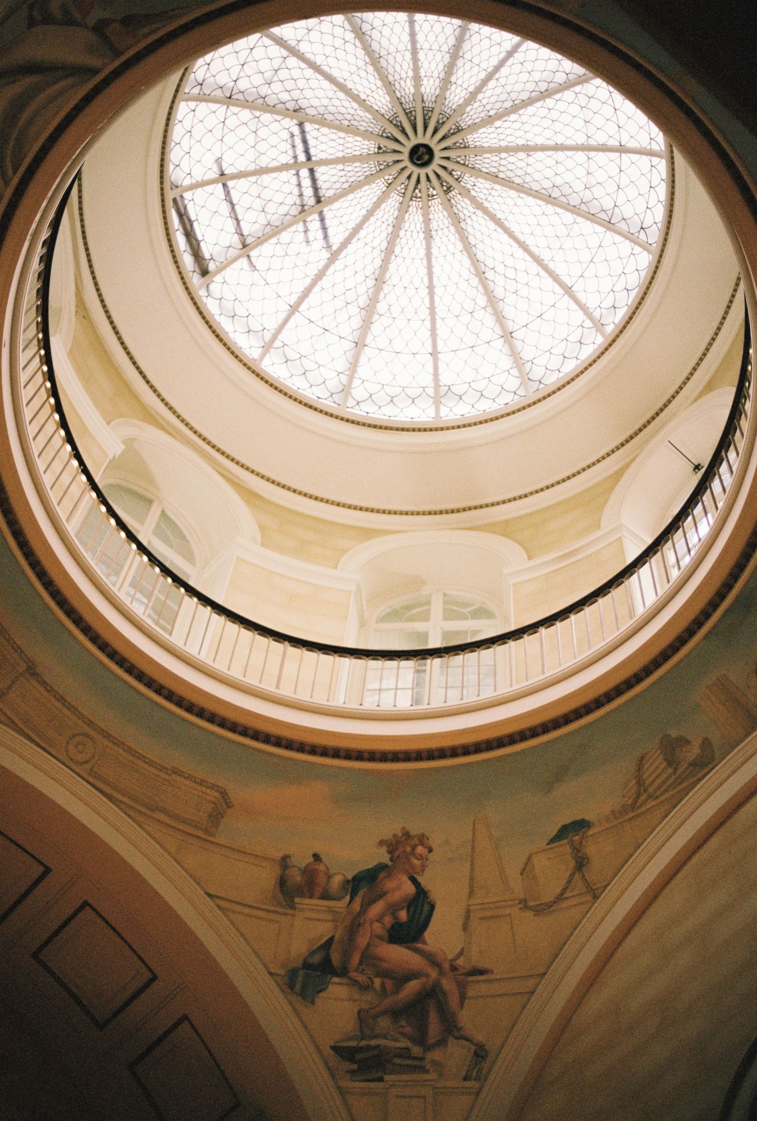 A domed ceiling with an intricate stained glass pattern and a central chandelier, with a mural painting on the walls.