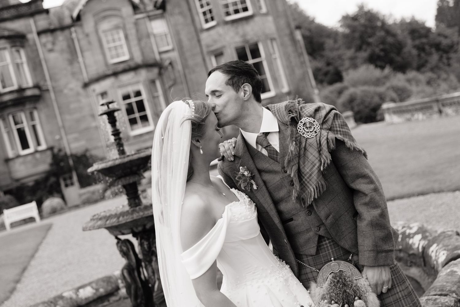Black and white photo of bride and groom kissing outside a historic Scottish manor house.