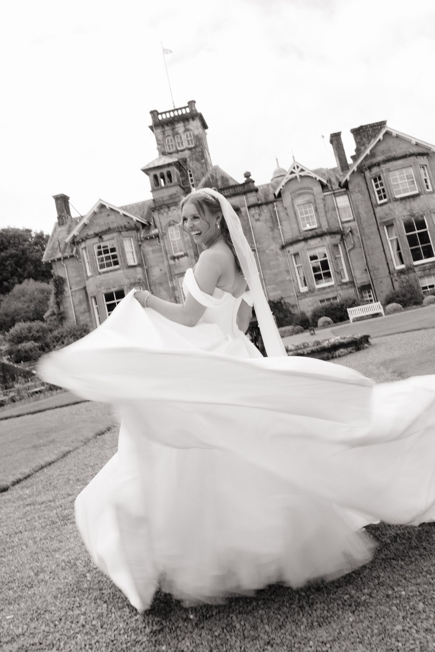 Bride twirling in white wedding gown outside a grand Scottish manor house, black and white photo.