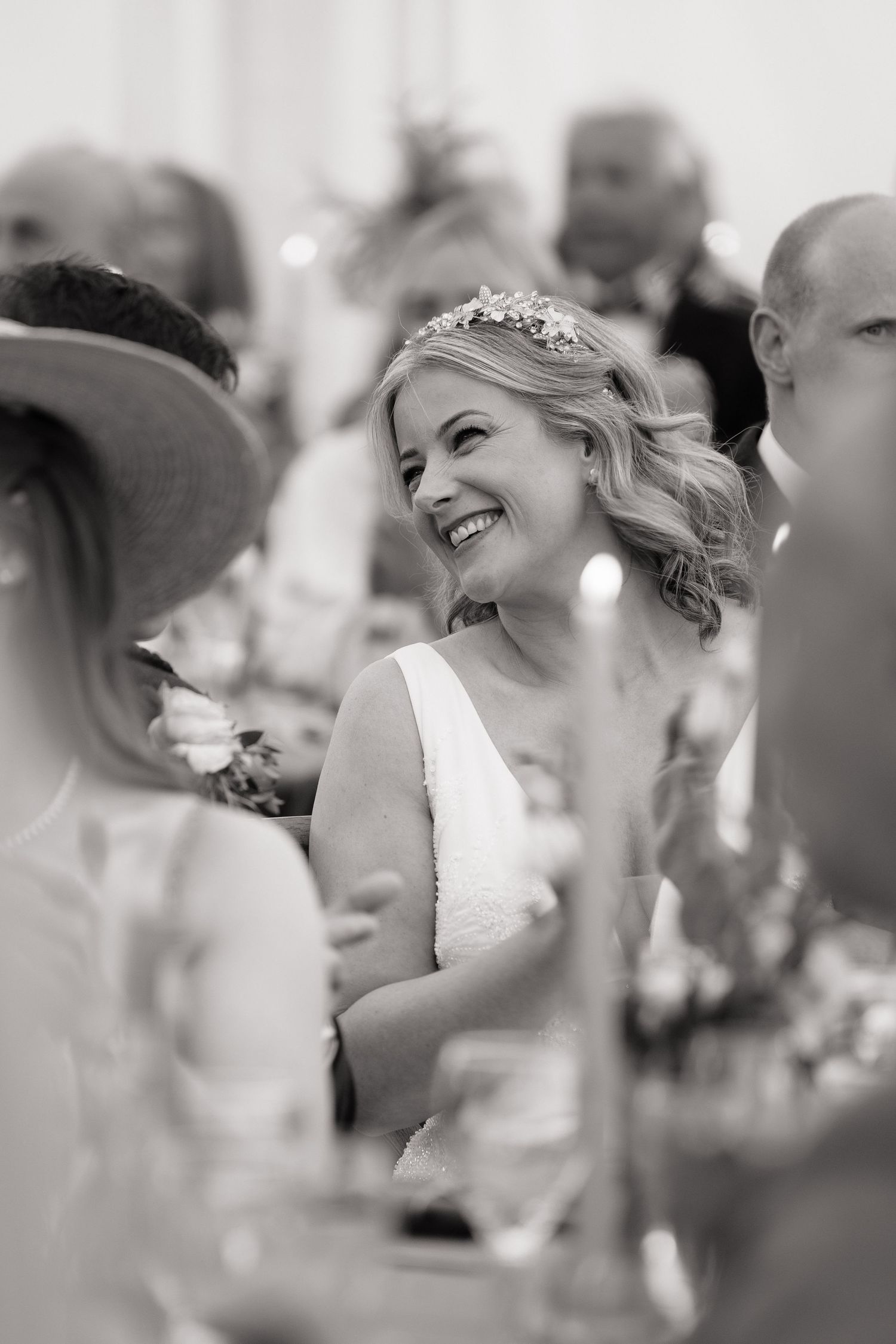 Black and white photo of a smiling bride wearing a floral hair accessory at her wedding reception.