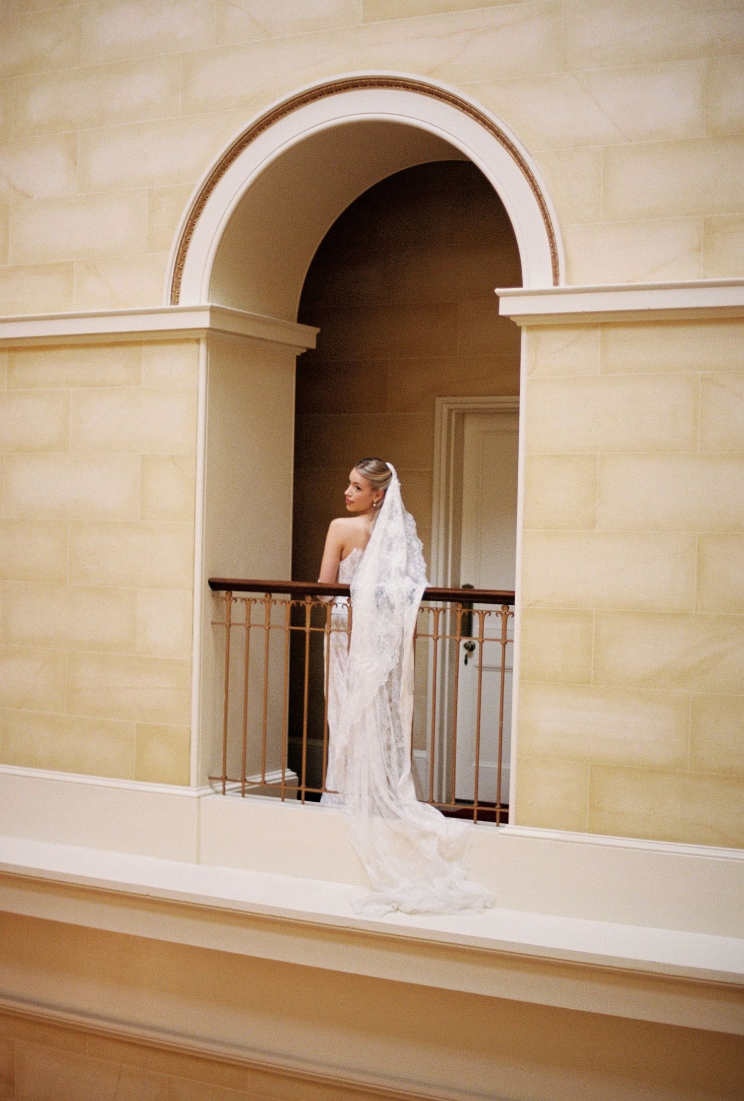 The image shows a bride in a white wedding dress and a groom in a black tuxedo standing in a formal setting.