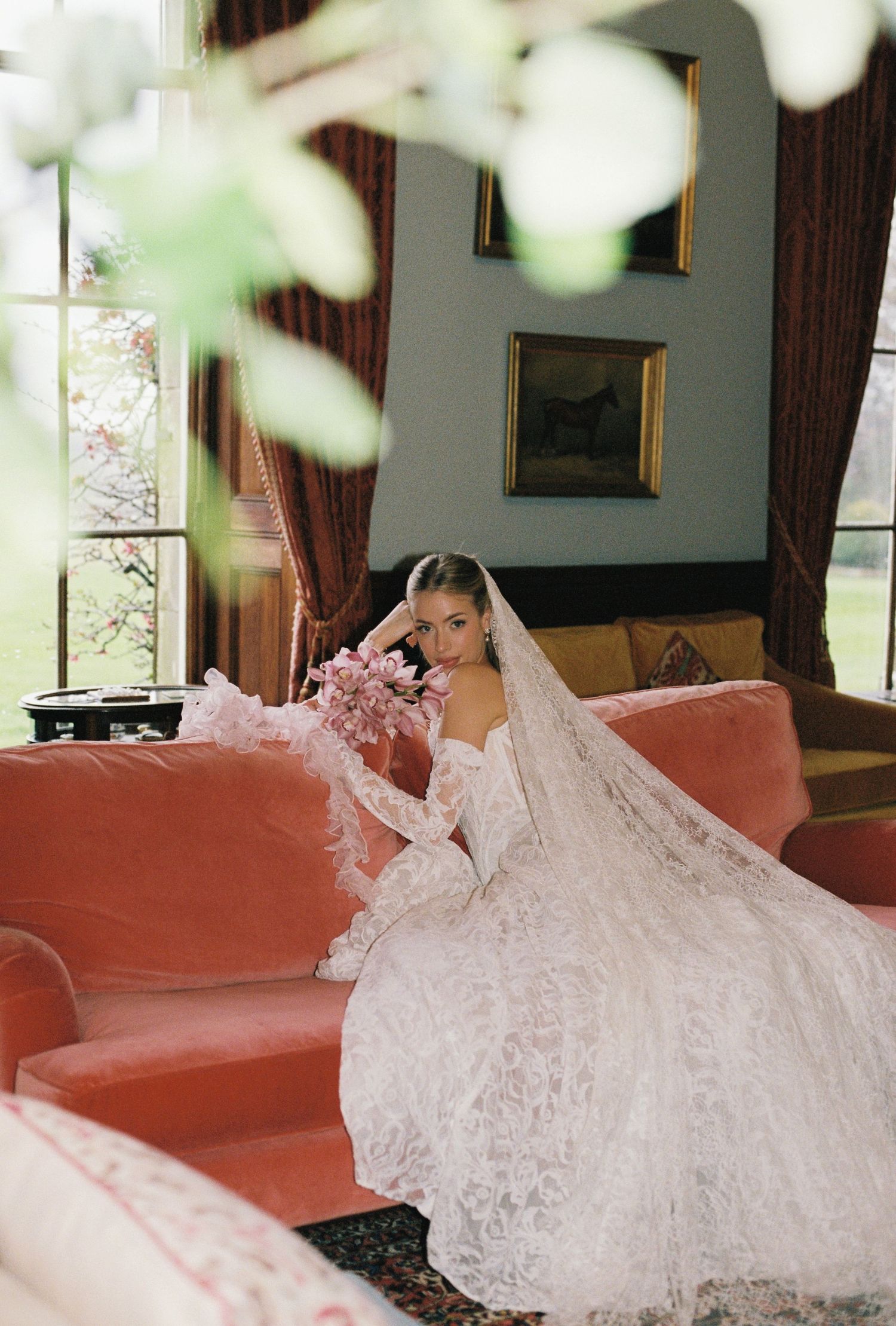 A bride in a white lace wedding dress sits on a couch in a wedding venue.