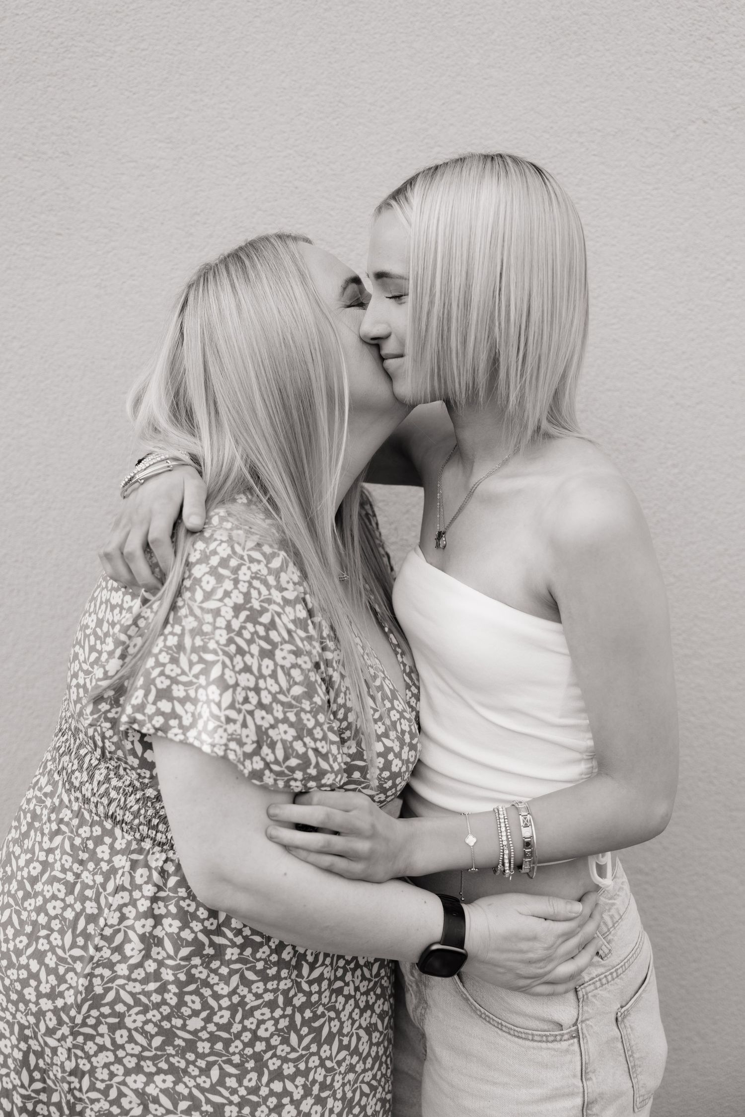 Two blonde women sharing a tender kiss while embracing in a black and white portrait photo.