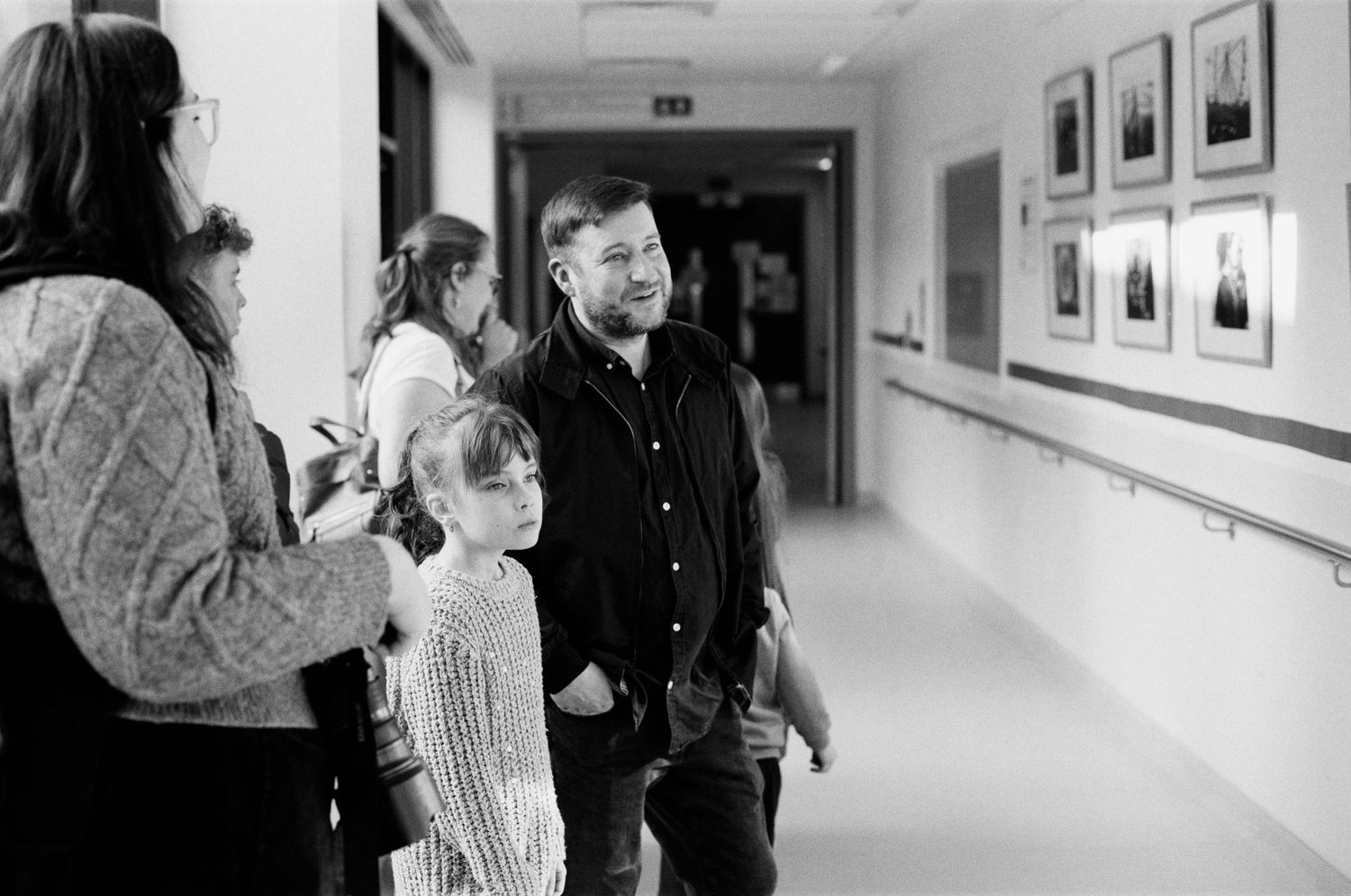 Man and child walking down a hallway with framed photos on the wall in black and white.