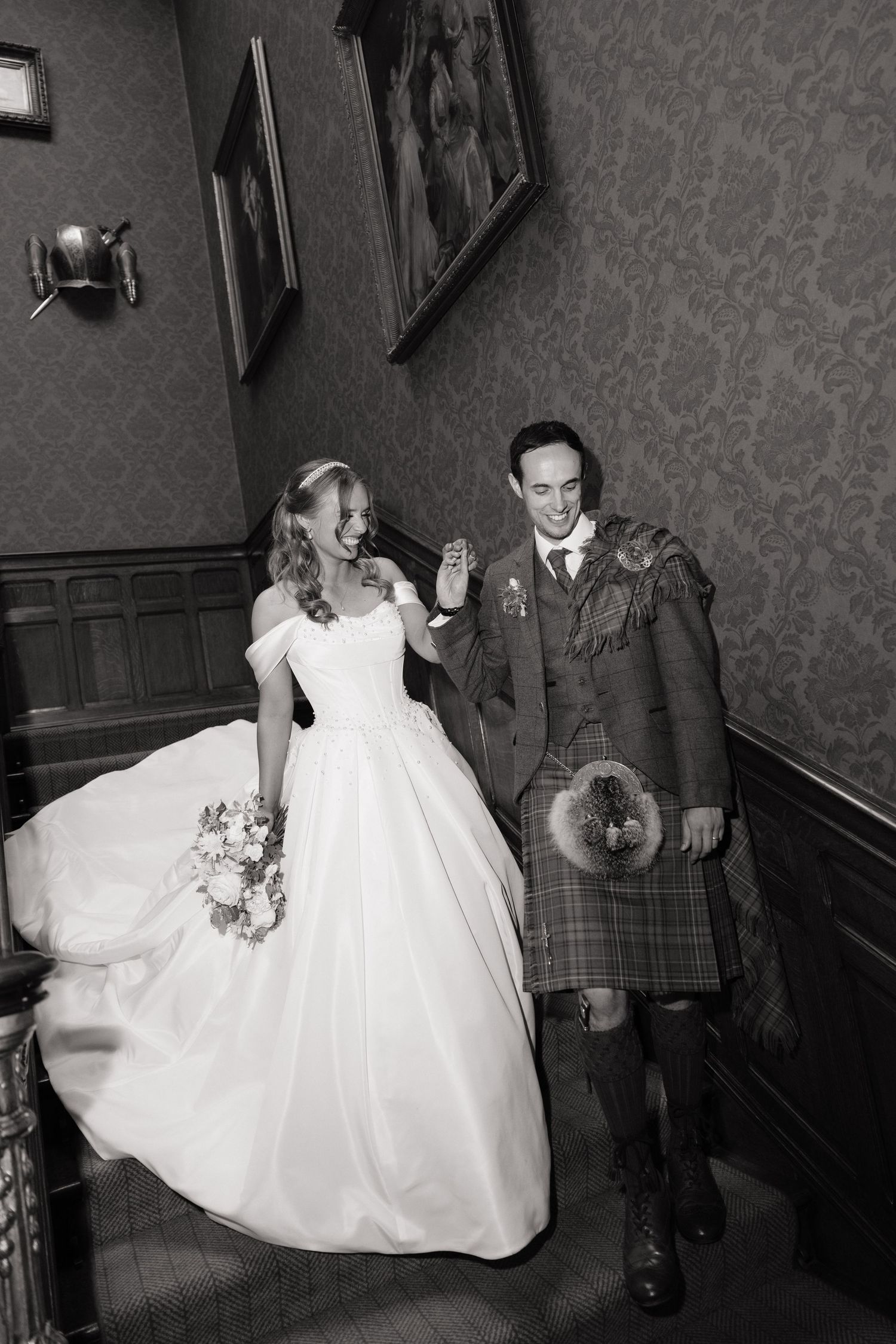 Bride and groom laugh together on ornate staircase in black and white wedding portrait.