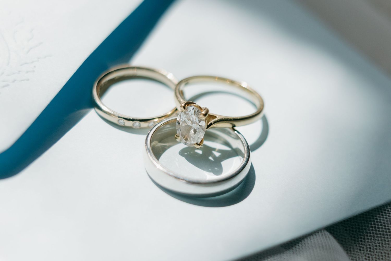 Three elegant wedding rings, including a diamond solitaire engagement ring, gold band, and silver band, resting together on a white surface.