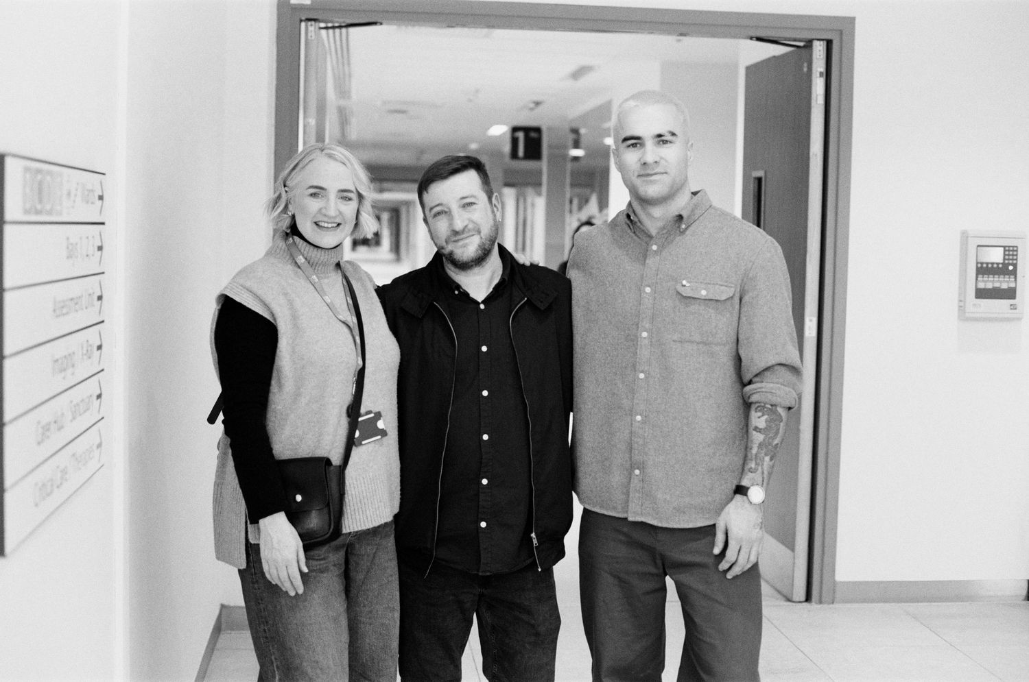 Three people posing together in a hallway, smiling for a black and white photo.