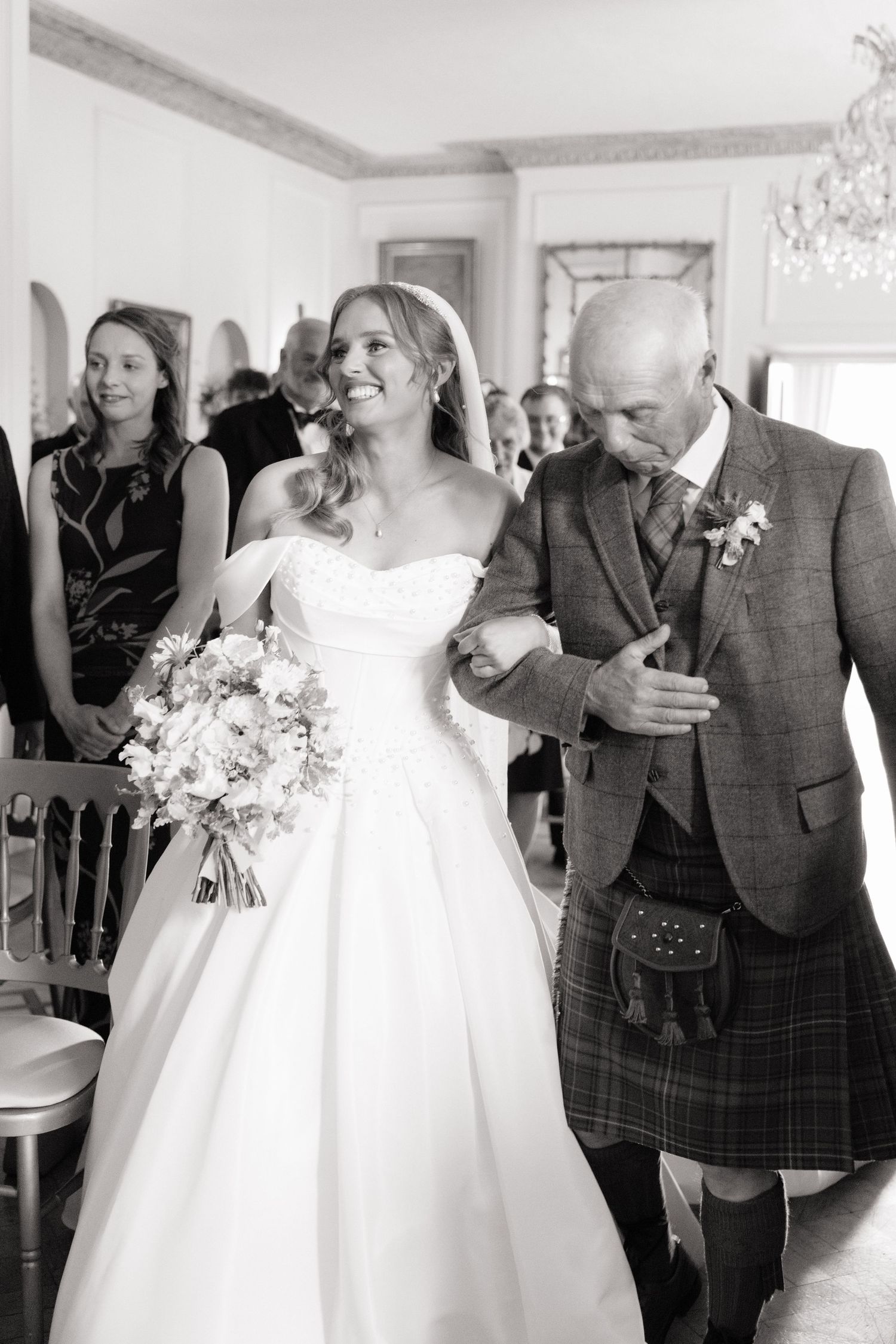 Black and white photo of radiant bride in ballgown walking down the aisle with her father.