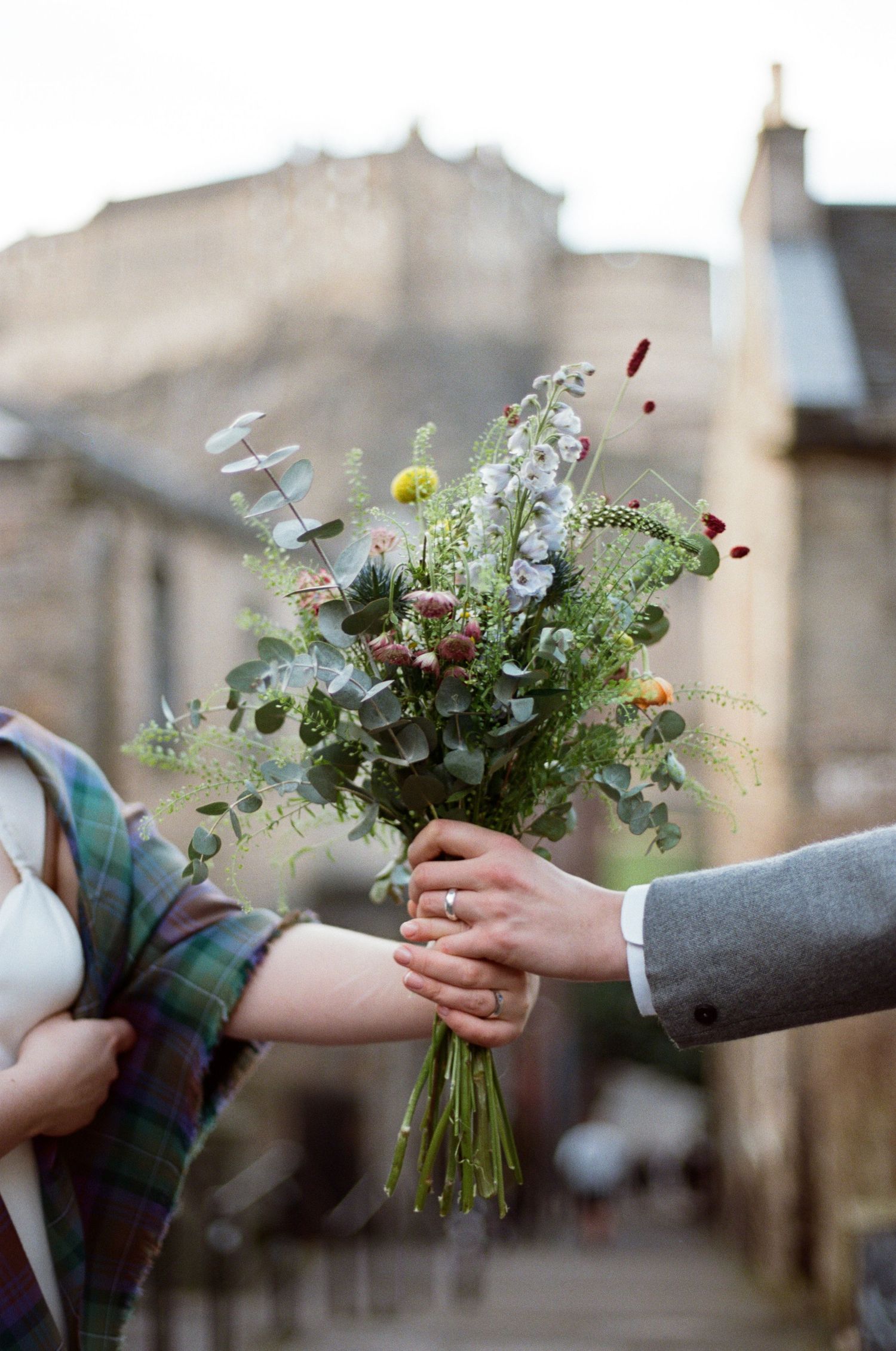 Couple holding a wild wedding bouquet with eucalyptus and mixed flowers on a cobblestone street in Edinburgh.