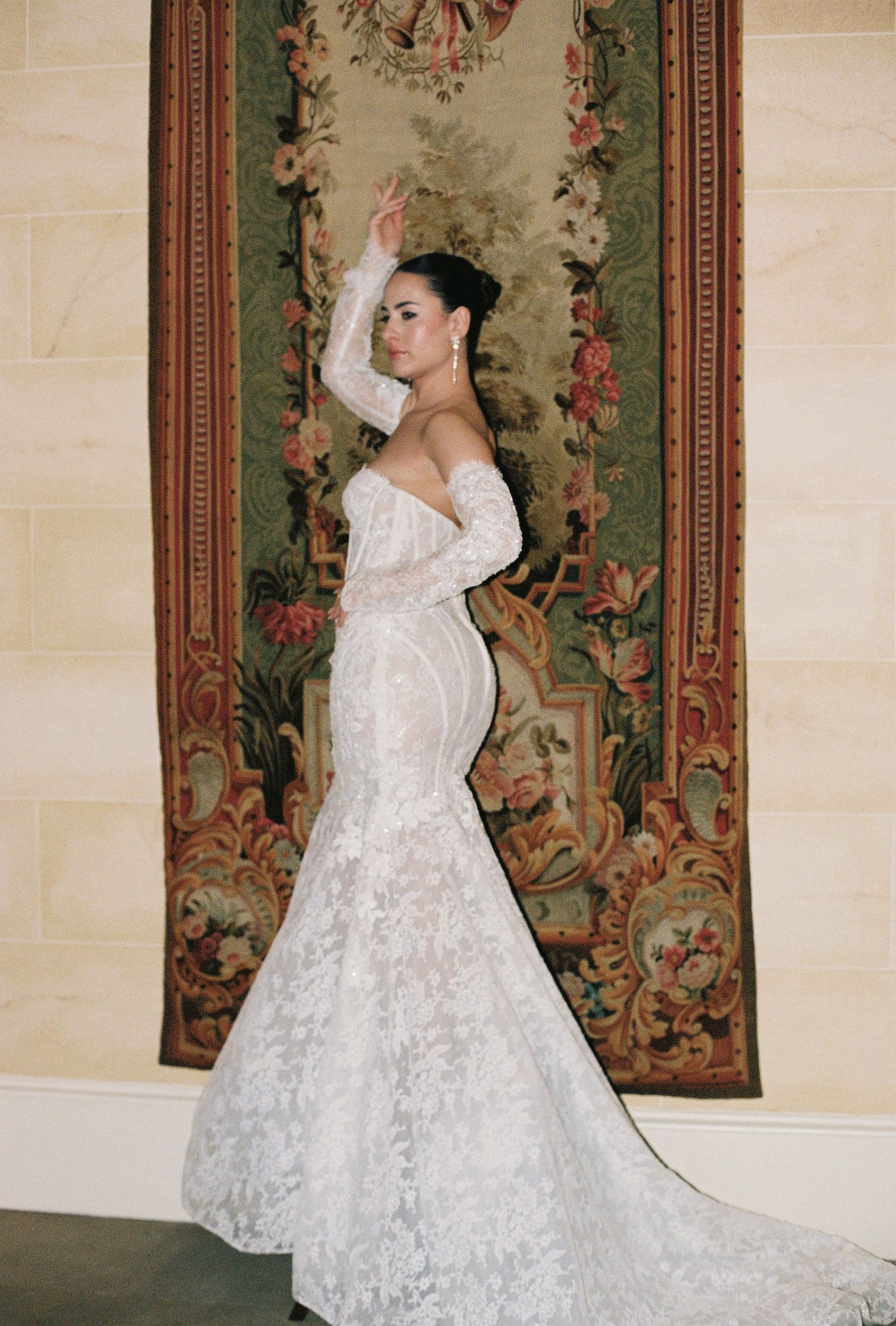 The image shows a woman in a white lace wedding dress standing in front of a floral-patterned backdrop.