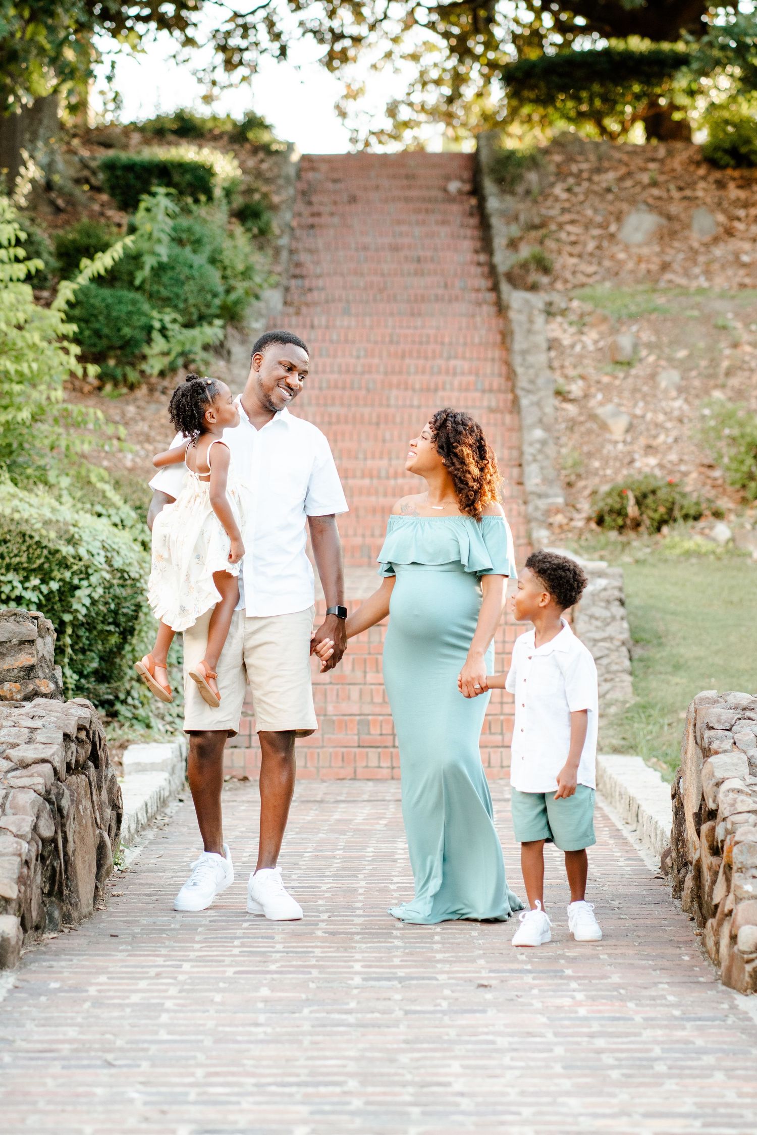 A family in coordinated white and mint outfits walks together on a brick pathway surrounded by greenery.
