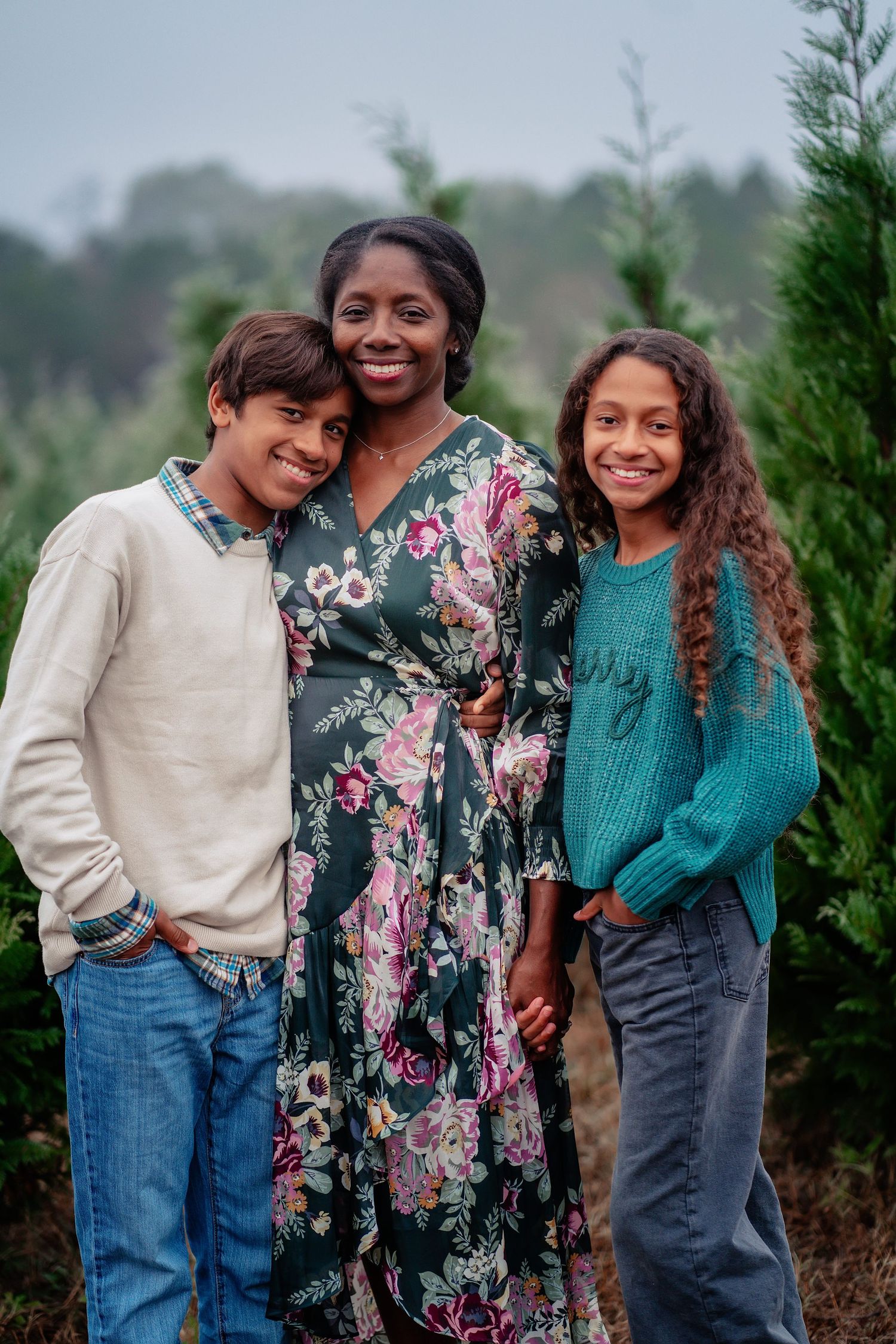 A family wearing coordinated outfits poses together among evergreen trees in an outdoor setting.