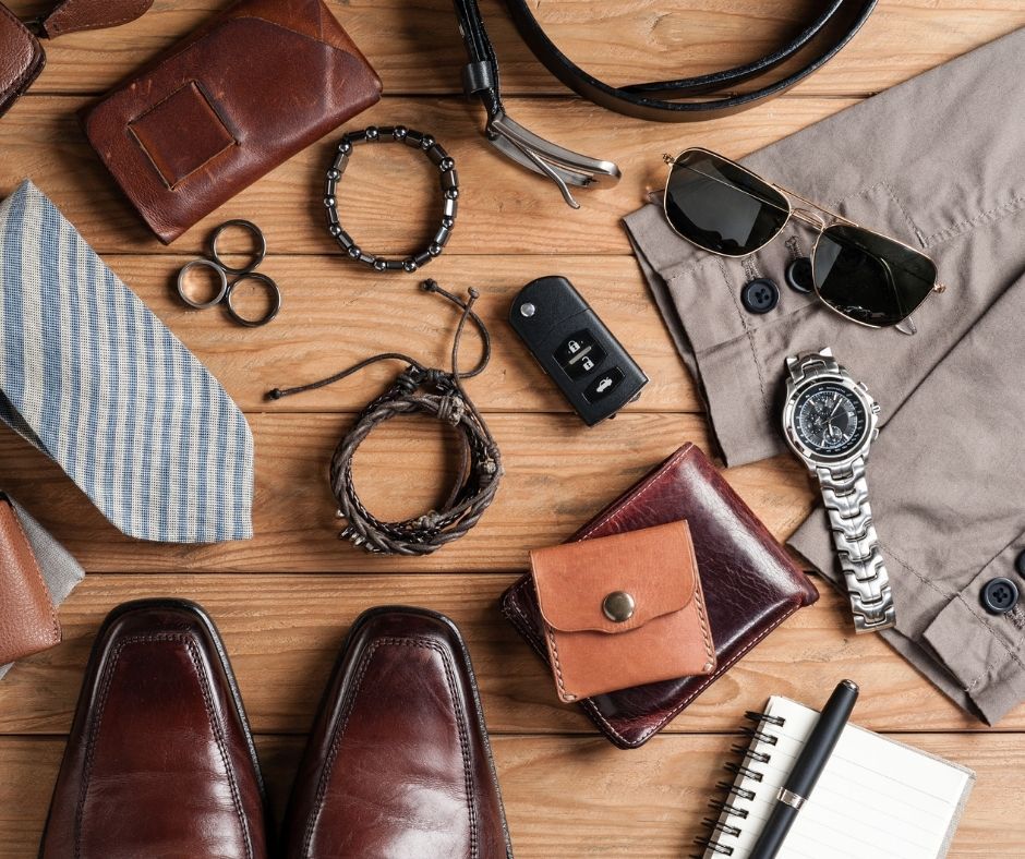 Flat lay of men's fashion accessories including leather shoes, wallet, watch and sunglasses on wooden background.