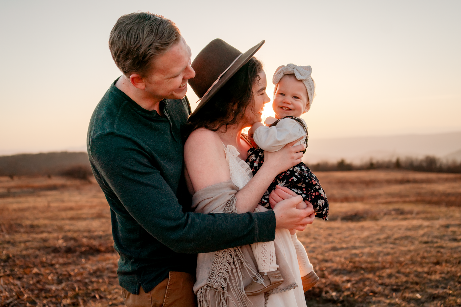 Parents sharing tender moments with baby during sunset photoshoot.