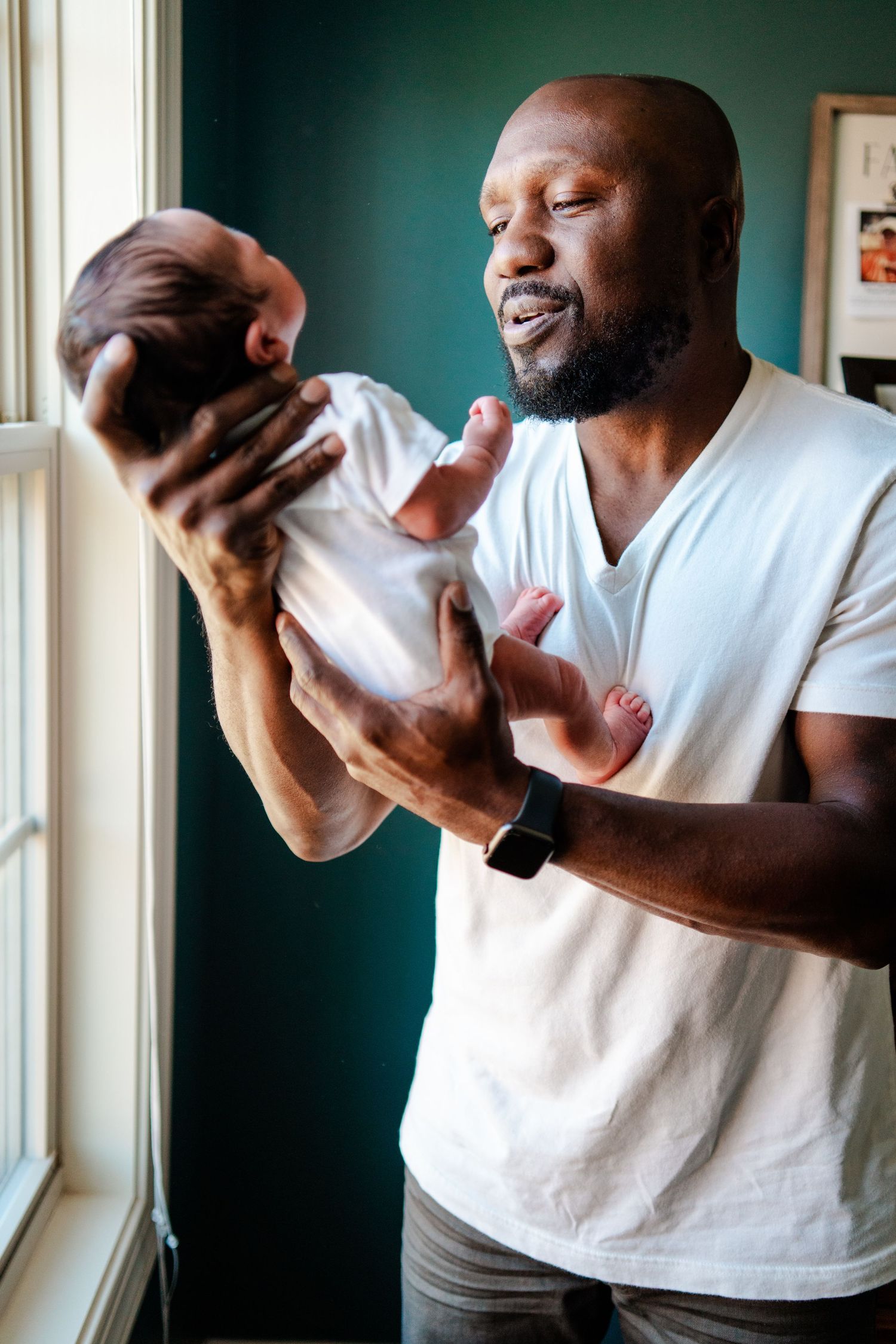 Loving parent holding and gazing at newborn baby near window with green wall.