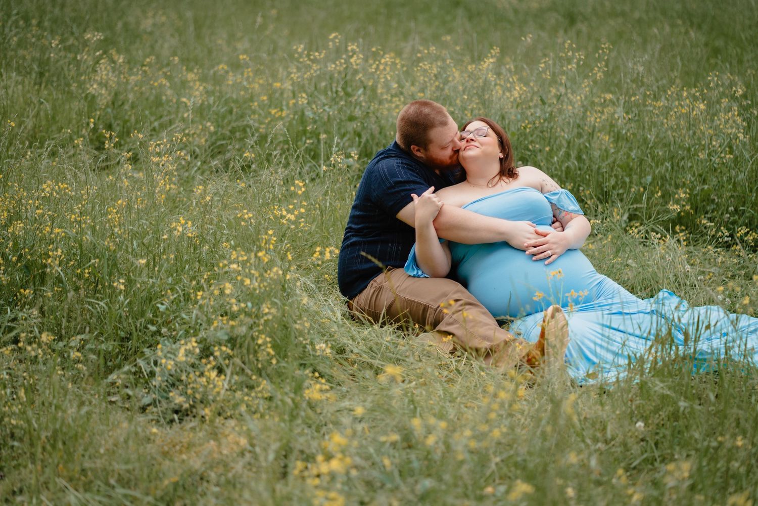 A couple embracing in a grassy field with yellow flowers.