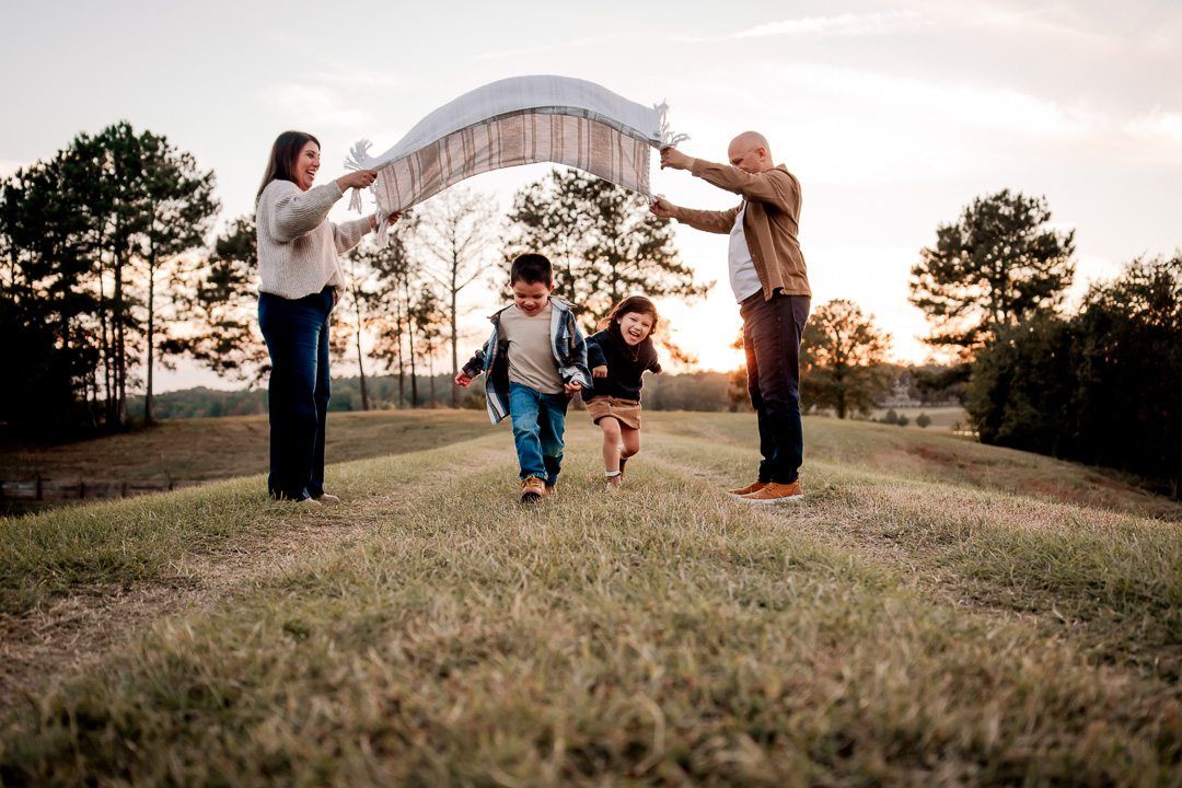 Family walking together on grassy hill during golden hour sunset.