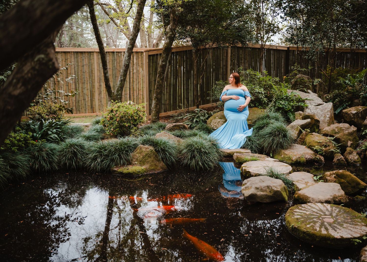 A person dressed in a blue costume stands in a garden pond surrounded by rocks and vegetation.