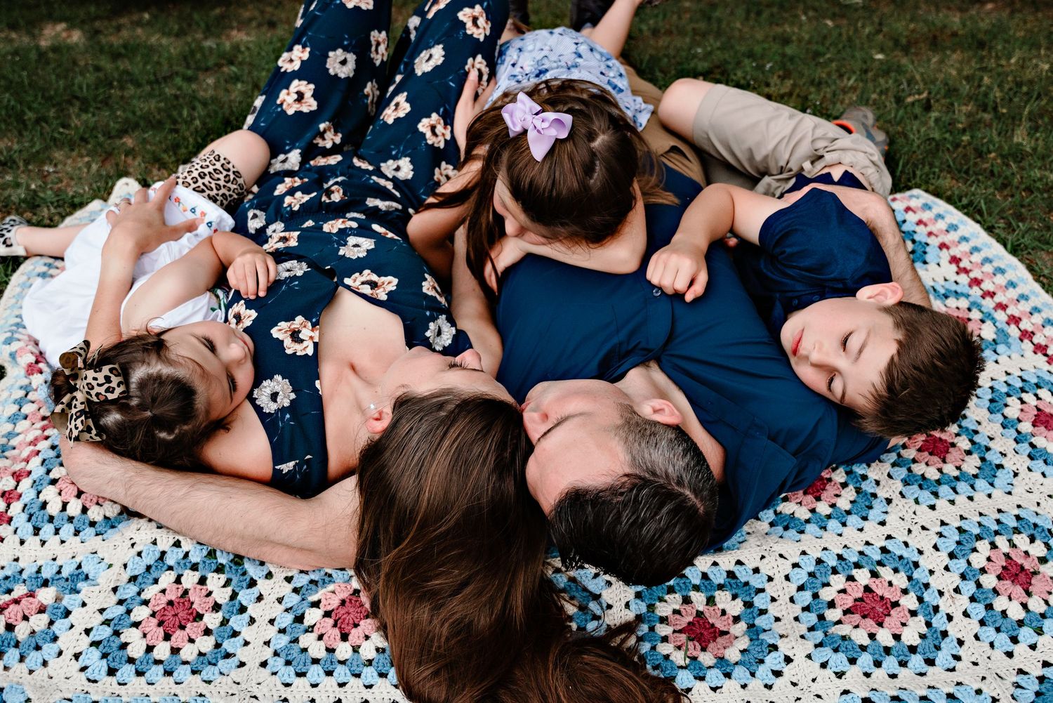 Family lying together on a patterned blanket in casual navy outfits.