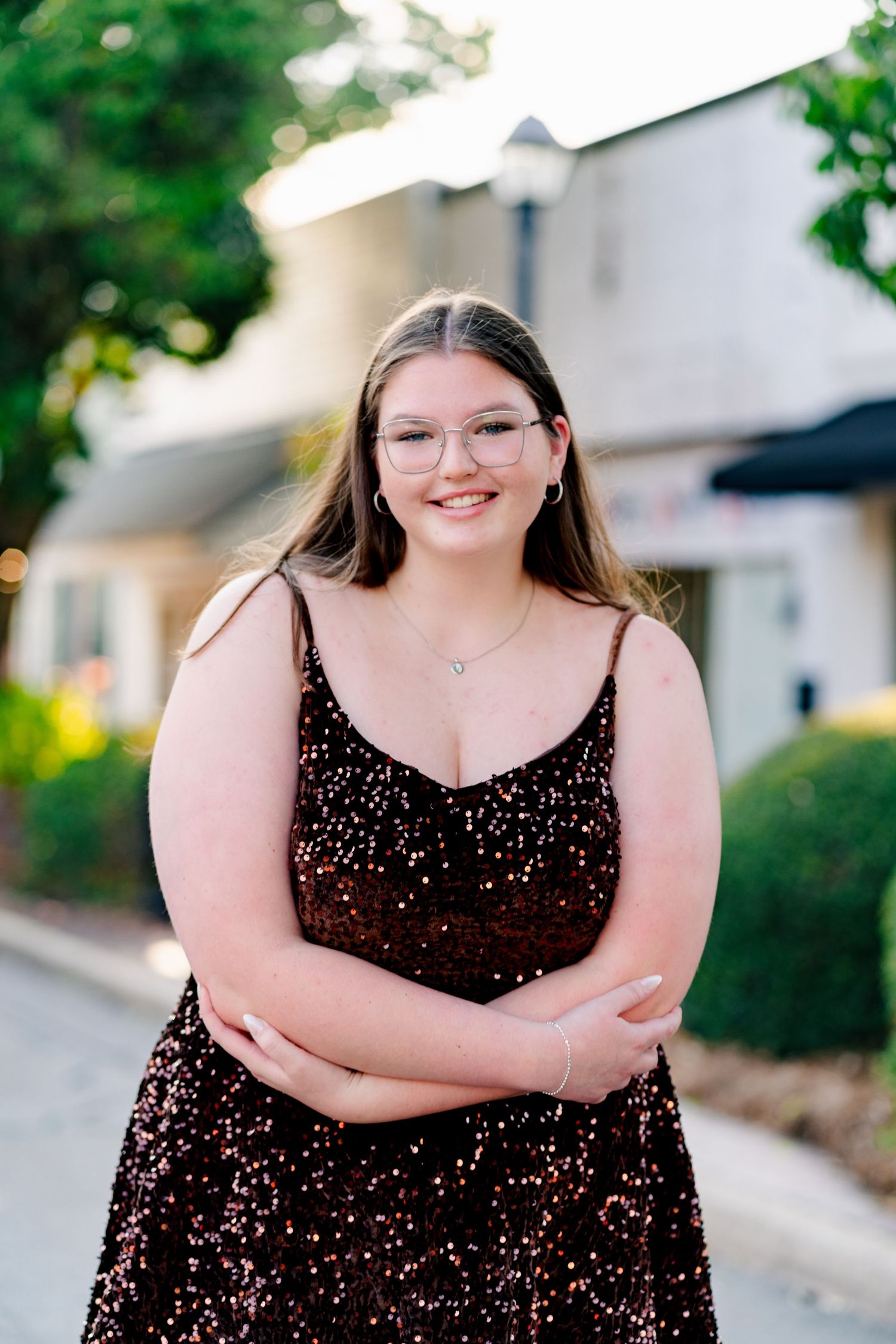 A person in a black sparkly dress poses outdoors in natural lighting during a photo session.