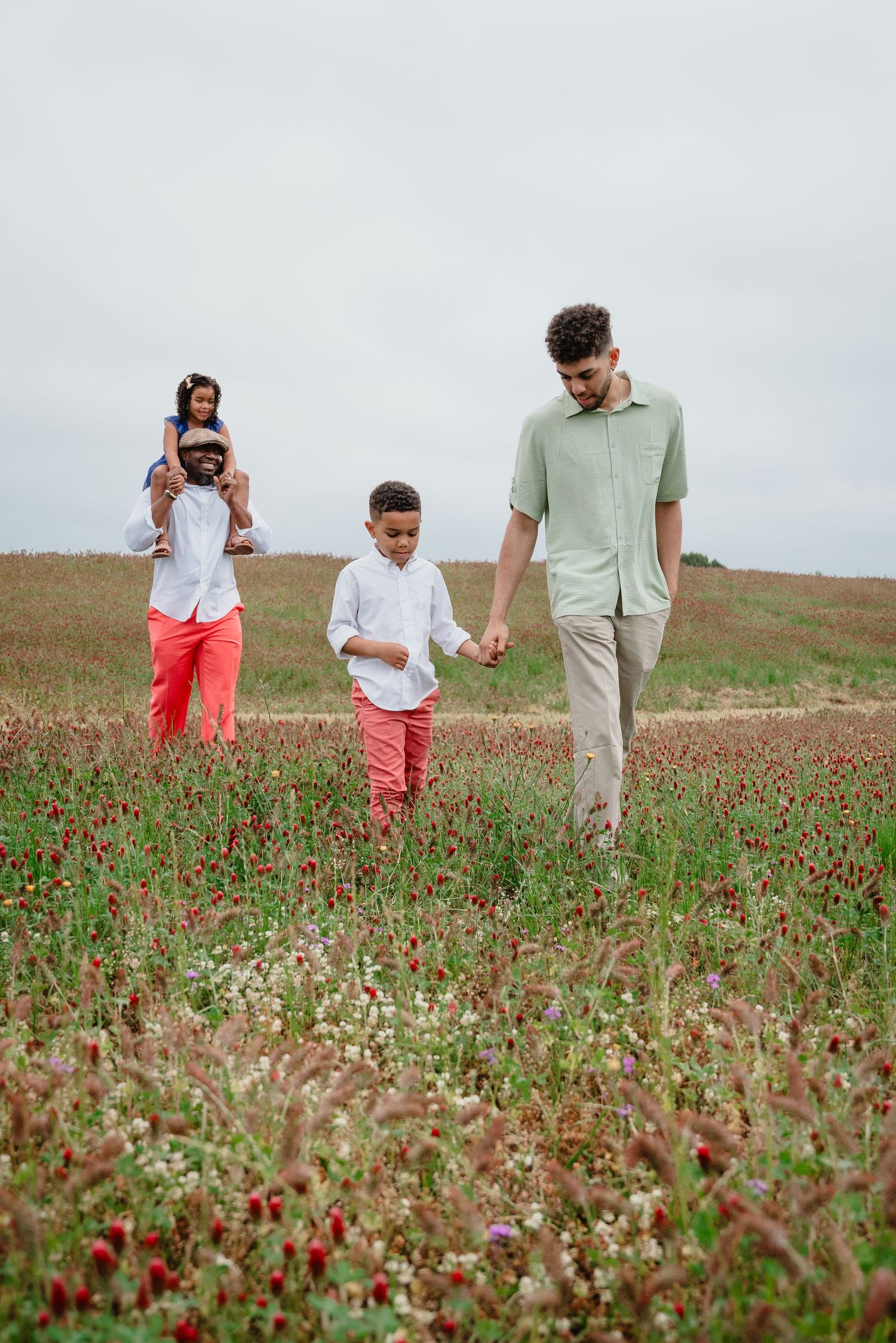 Family walking through blooming crimson clover field during cloudy day photoshoot.