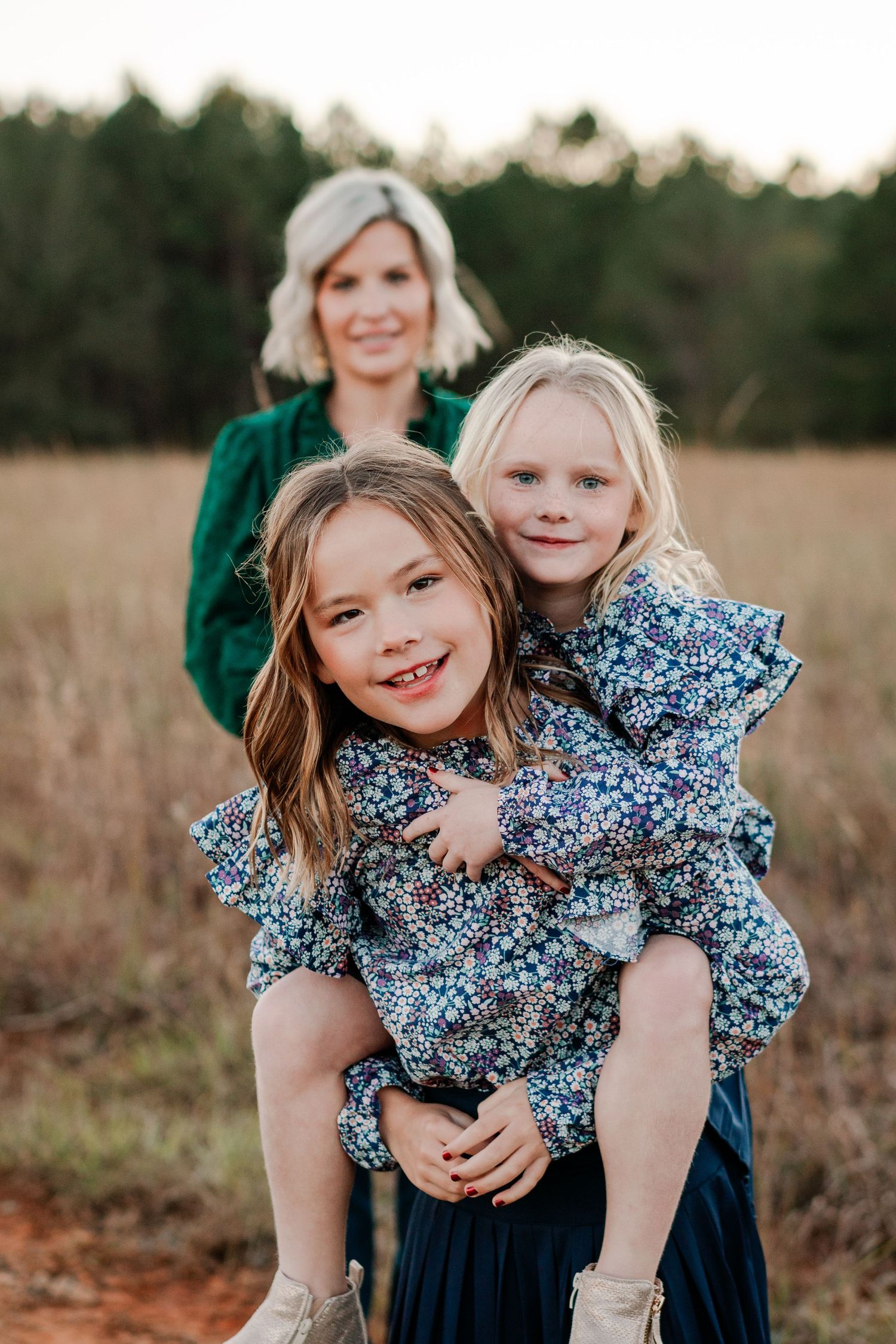 A playful outdoor family portrait with coordinating blue floral dresses in a golden field.