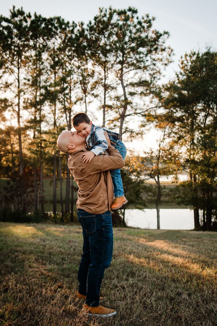 A tender moment between parent and child silhouetted against tall pine trees at sunset.