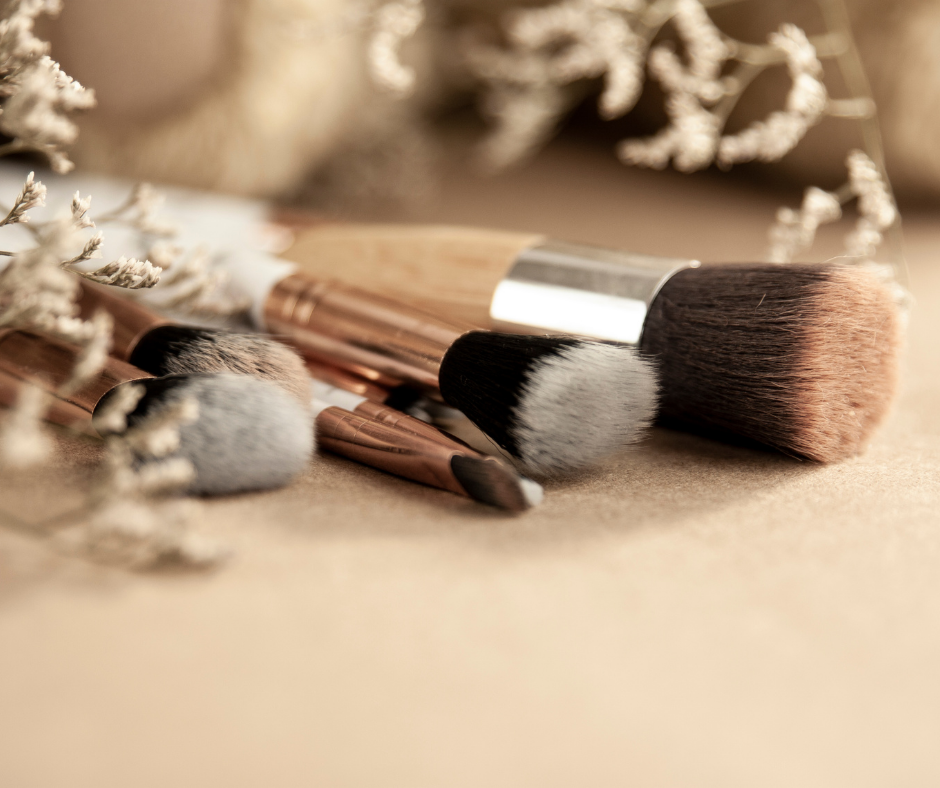 Professional makeup brushes with soft bristles arranged on beige surface with delicate dried flowers in warm tones.