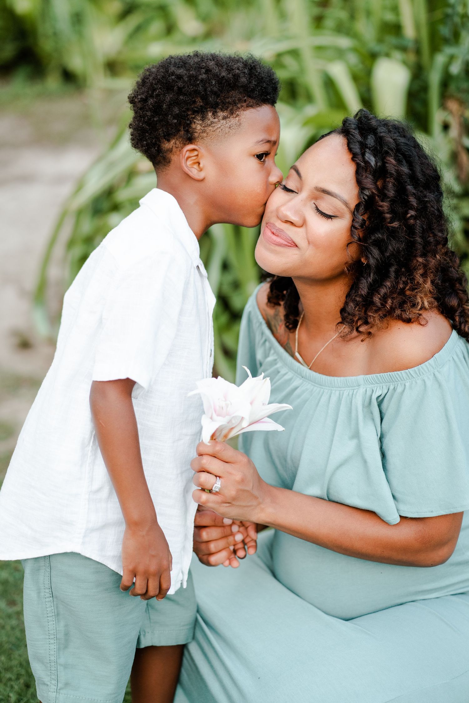 A tender moment between parent and child outdoors, with a white flower held between them in a natural garden setting.